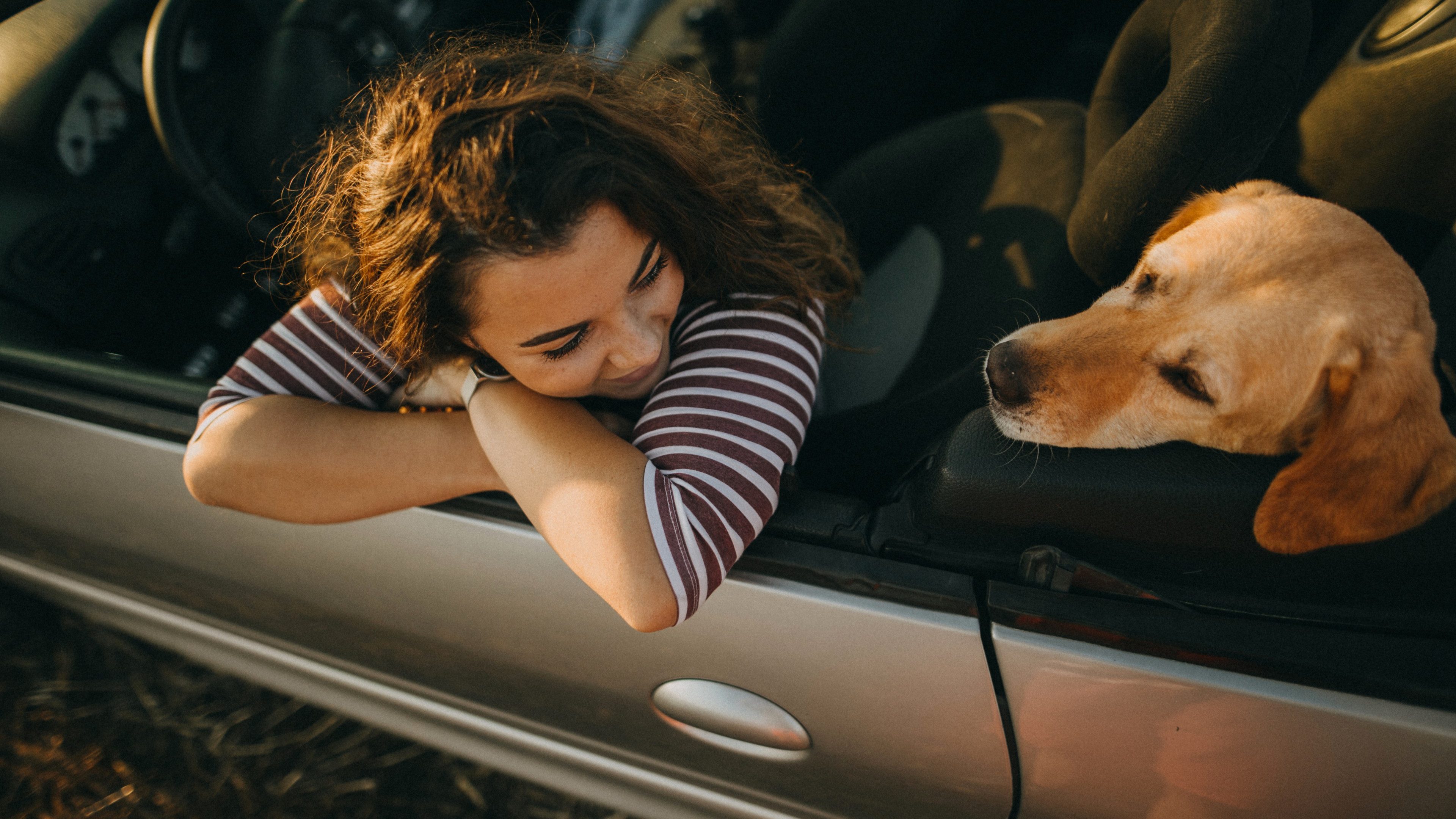 A woman sits in her car looking at her dog in the backseat.