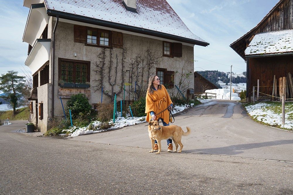 A woman with a dog stands in front of a house.
