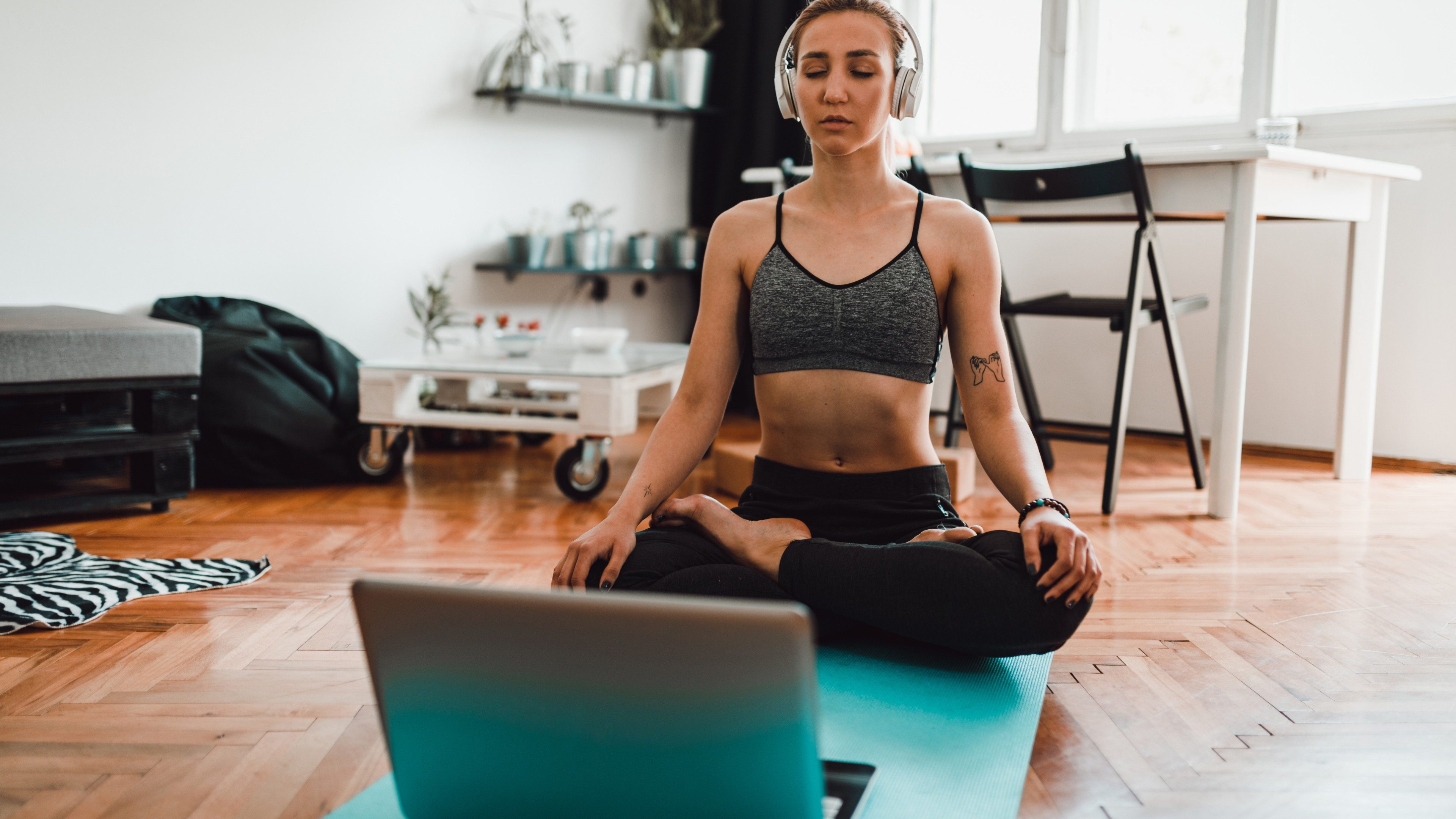 Beautiful young woman using laptop and headphones while meditating and practicing yoga at home