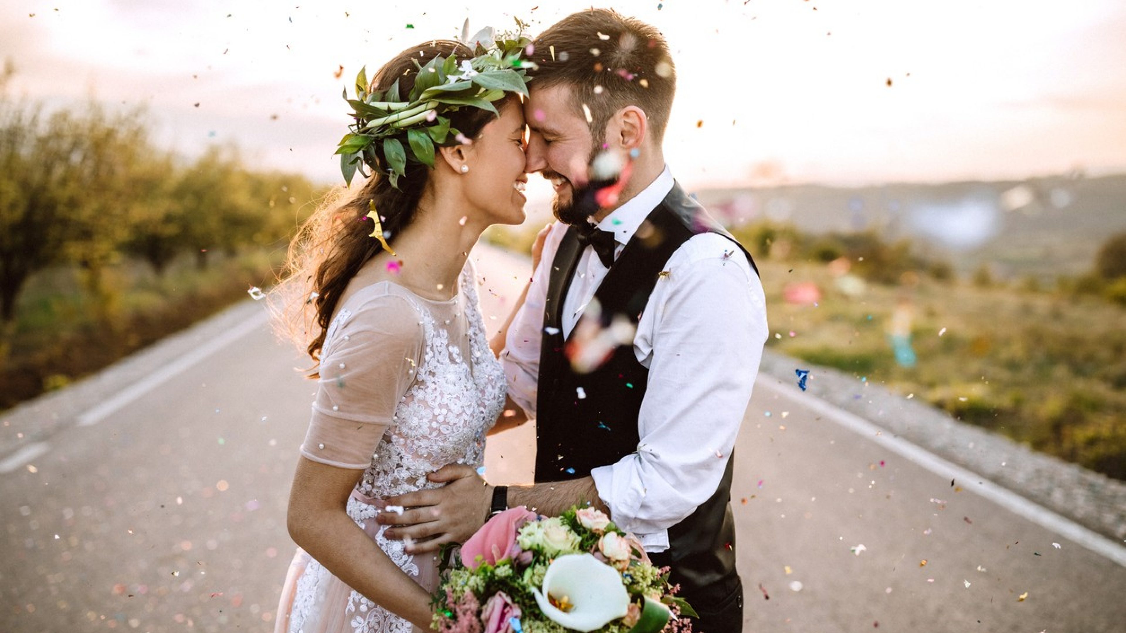 Verliebtes Hochzeitspaar in Hochzeitskleid und Hochzeitsanzug steht auf einer Strasse, vor ihm wird Konfetti in die Luft geworfen.