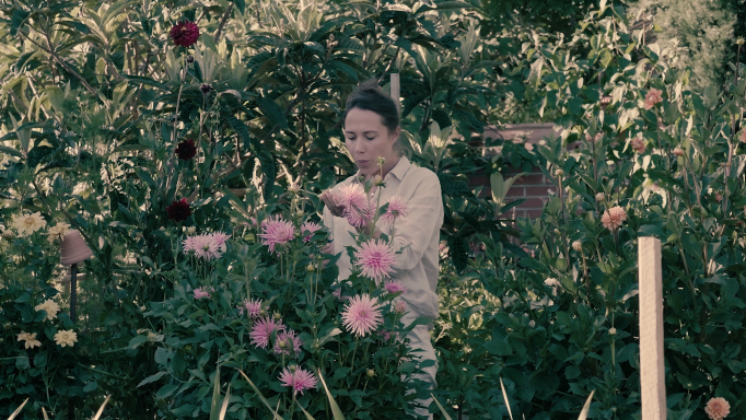 Eine Frau steht im Garten umringt von Pflanzen.