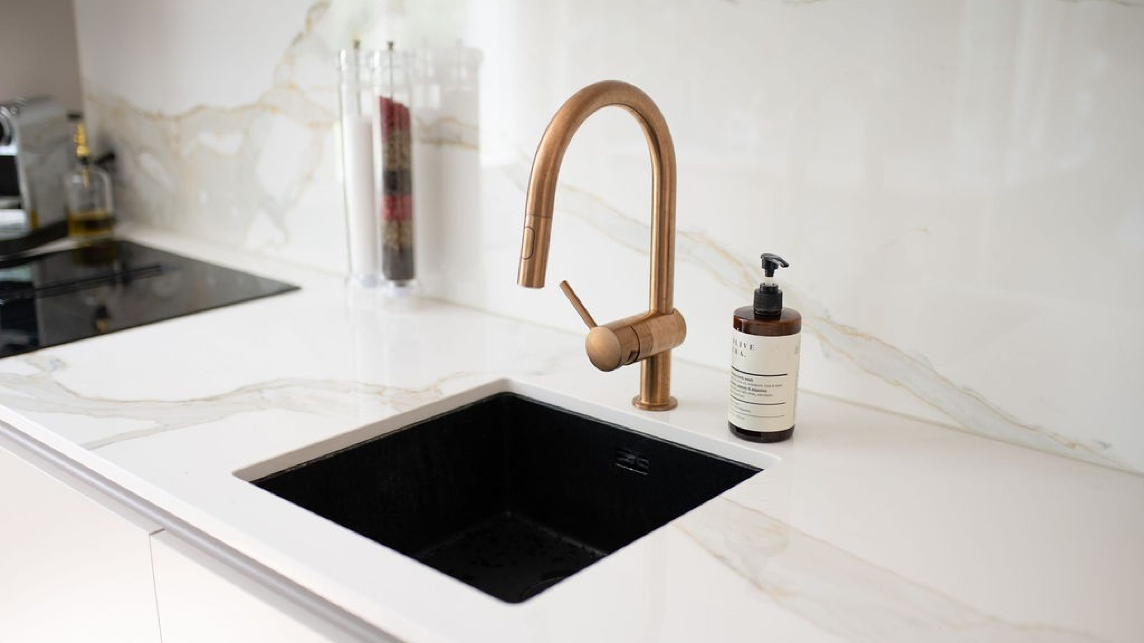 In einer weissen Marmorküche ist ein Lavabo mit goldgebürsteter Armatur und schwarzem Spülbecken eingebaut.