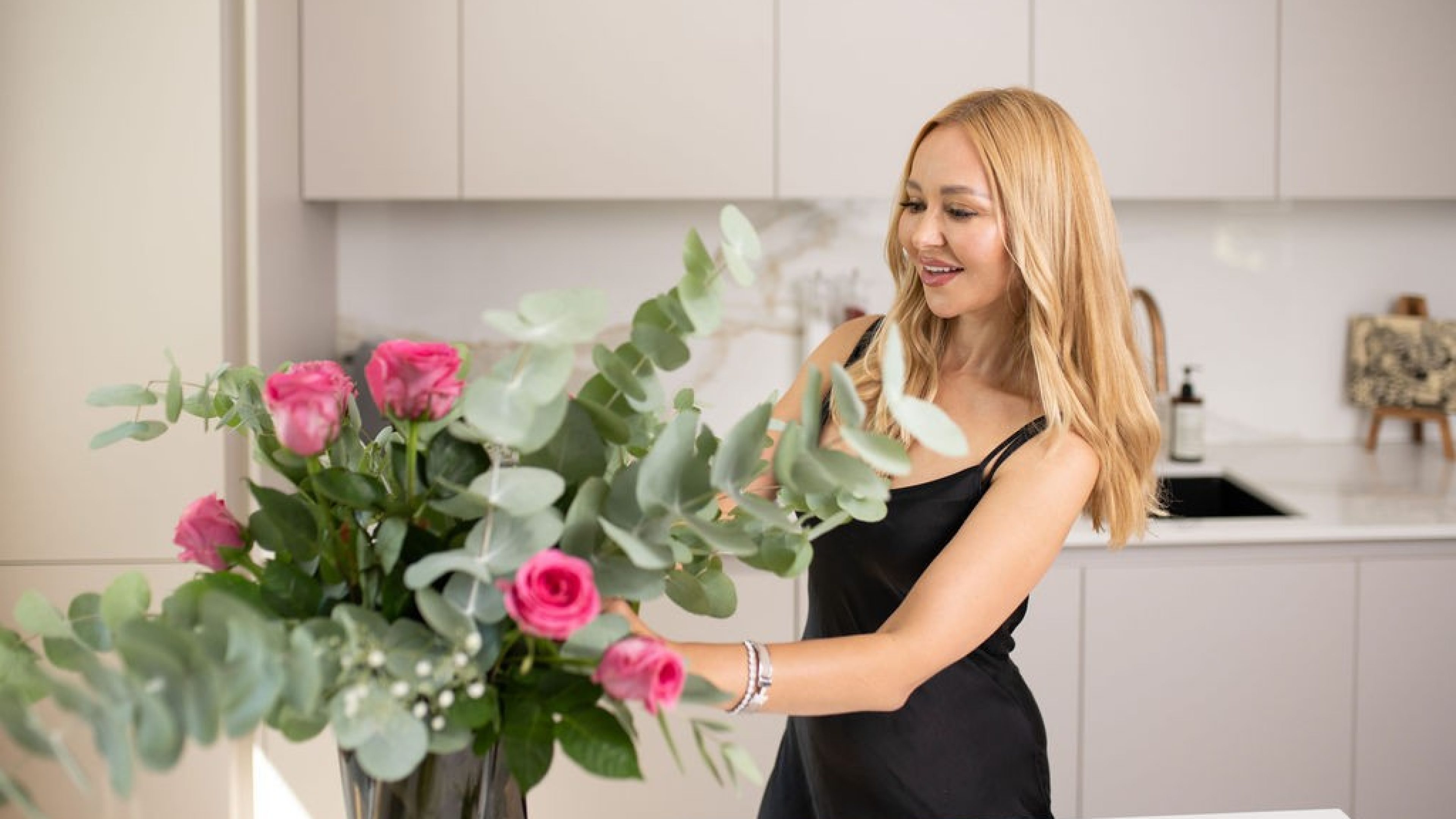 Eine Frau richtet in ihrer hellen Küche einen prächtigen Strauss mit Rosen und Eukalyptus.