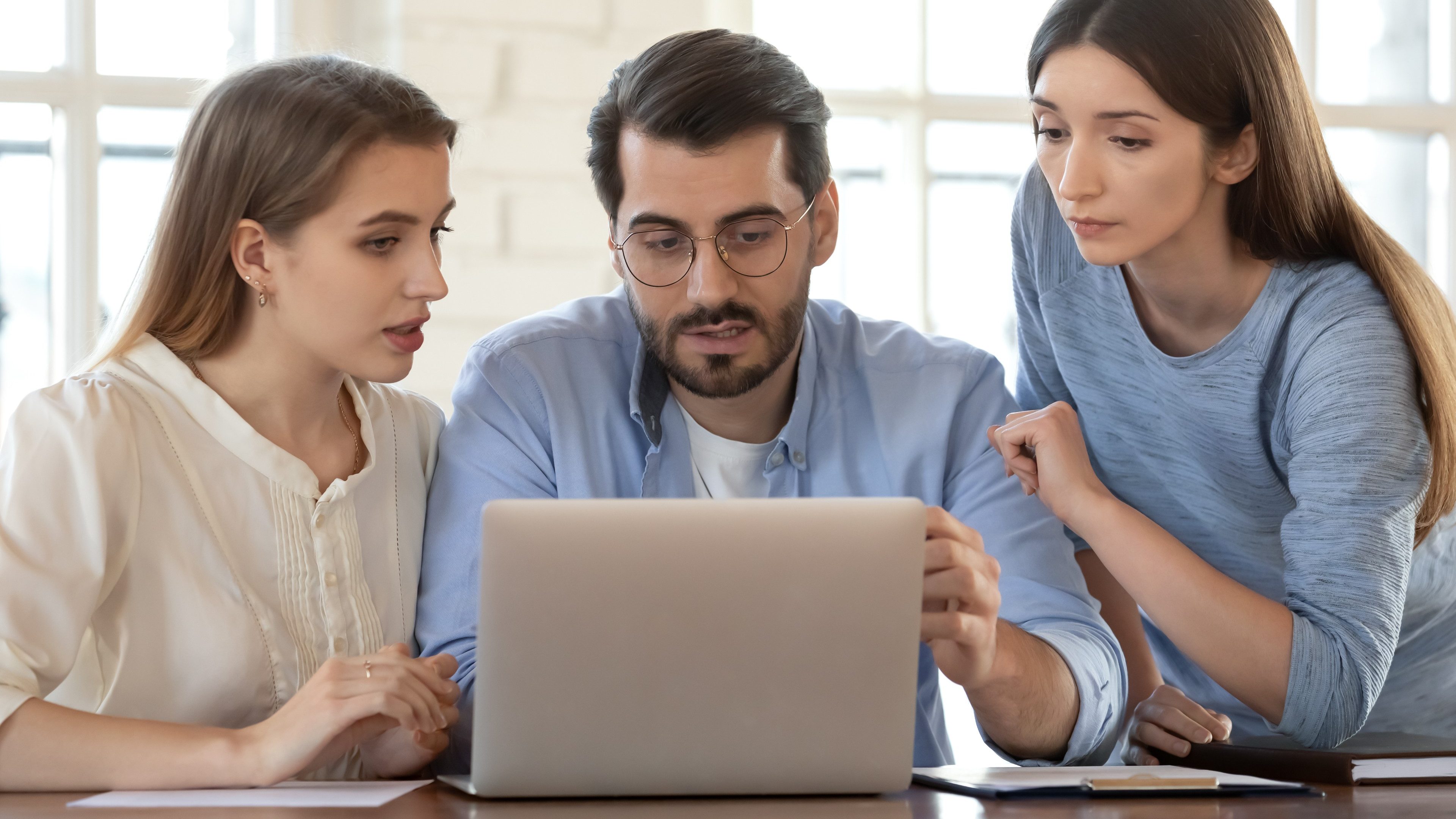 Businesswoman realtor consulting young couple at meeting, using laptop, pointing finger at screen, demonstrating presentation, man and woman discussing mortgage or loan conditions with manager