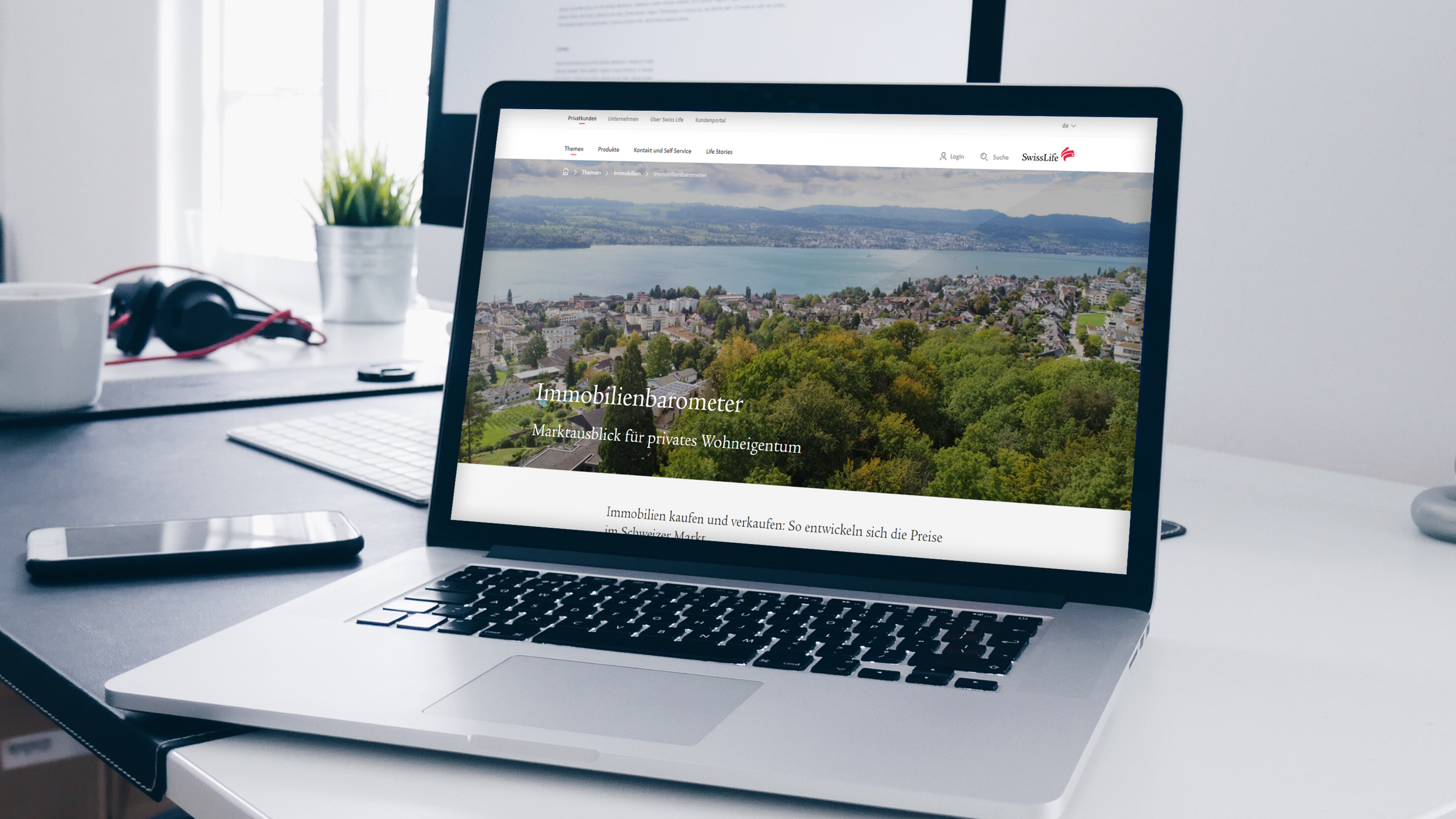 Auf dem Schreibtisch steht ein geöffneter Laptop, auf welchem die SwissLife Immobilienbarometerseite abgebildet ist: ein See, Häuser und Bäume.