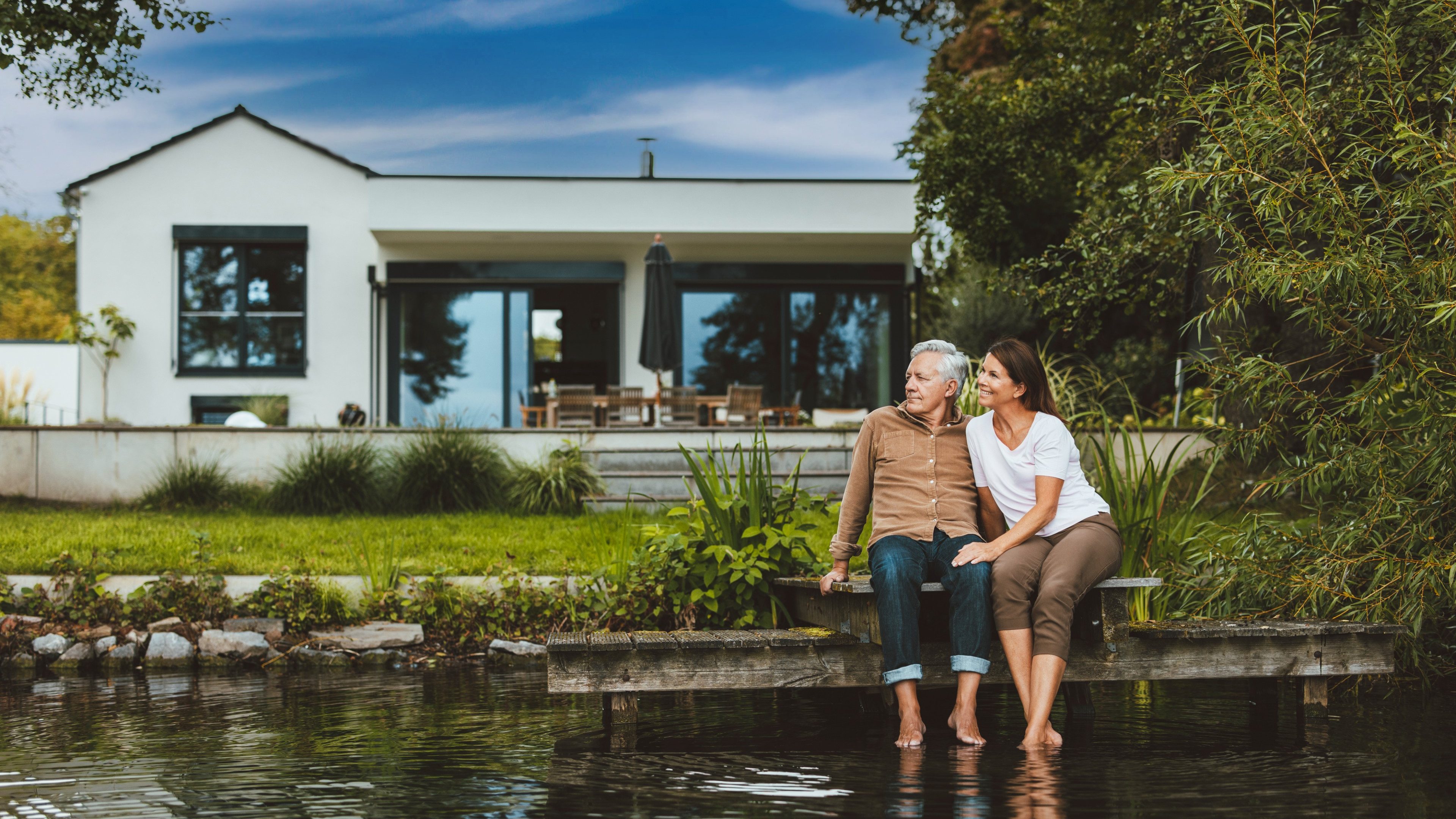 Smiling woman with man sitting on jetty by lake at backyard