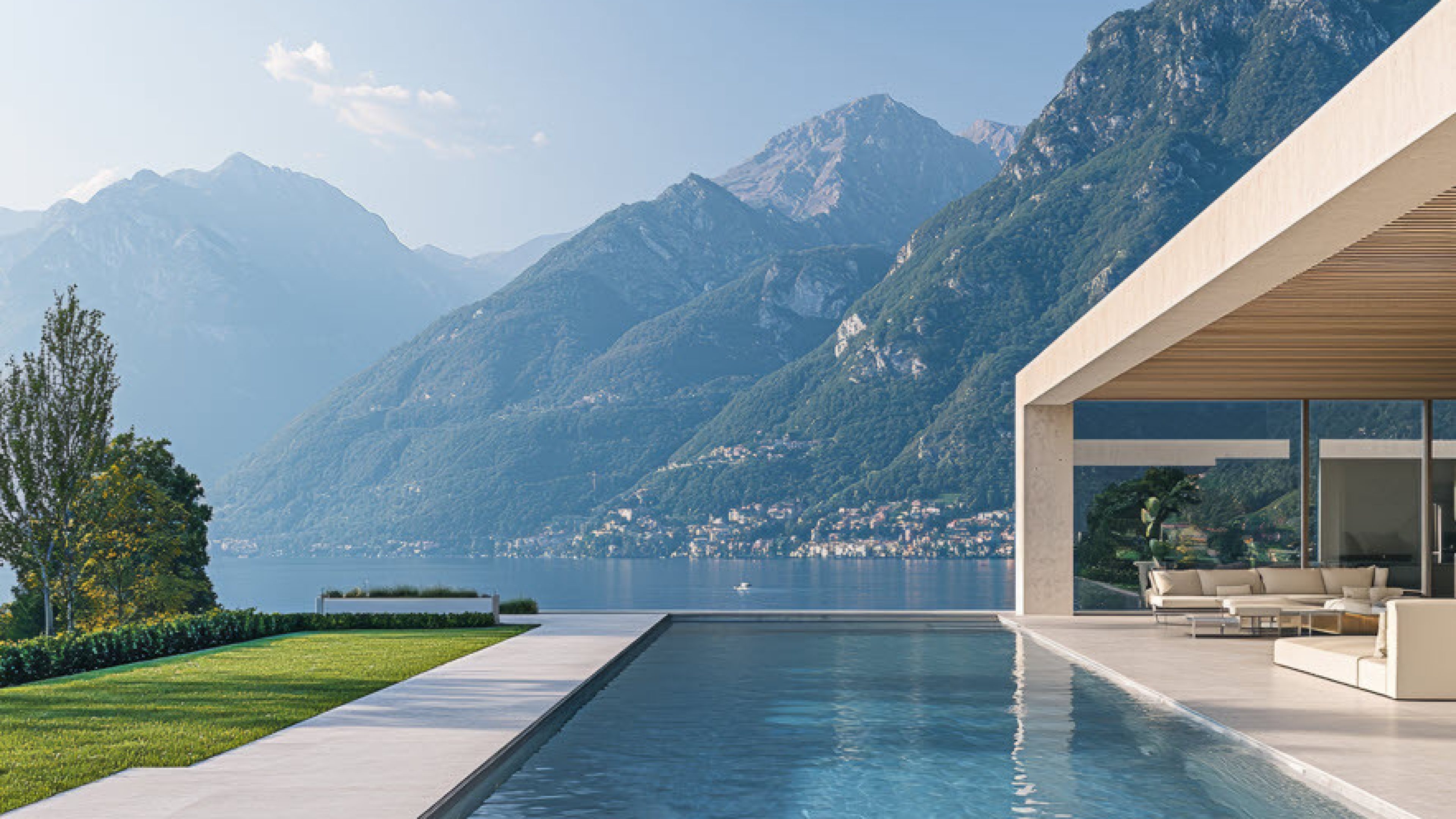 gedeckter Sitzplatz mit weissen Polstermöbel, grosser Pool und Sicht auf den See und in die Berge