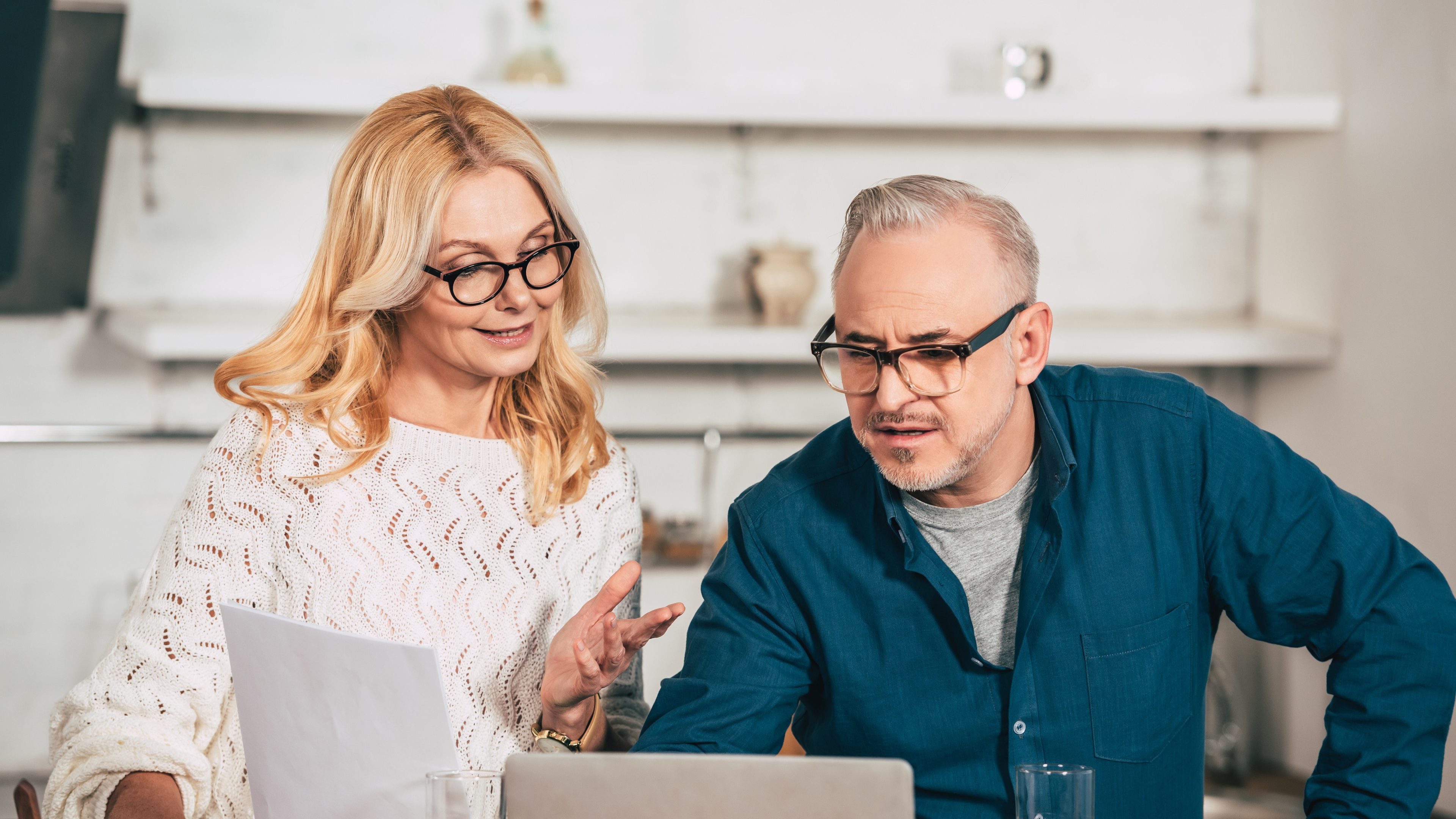 attractive woman holding blank paper and standing with husband in eye glasses near laptop