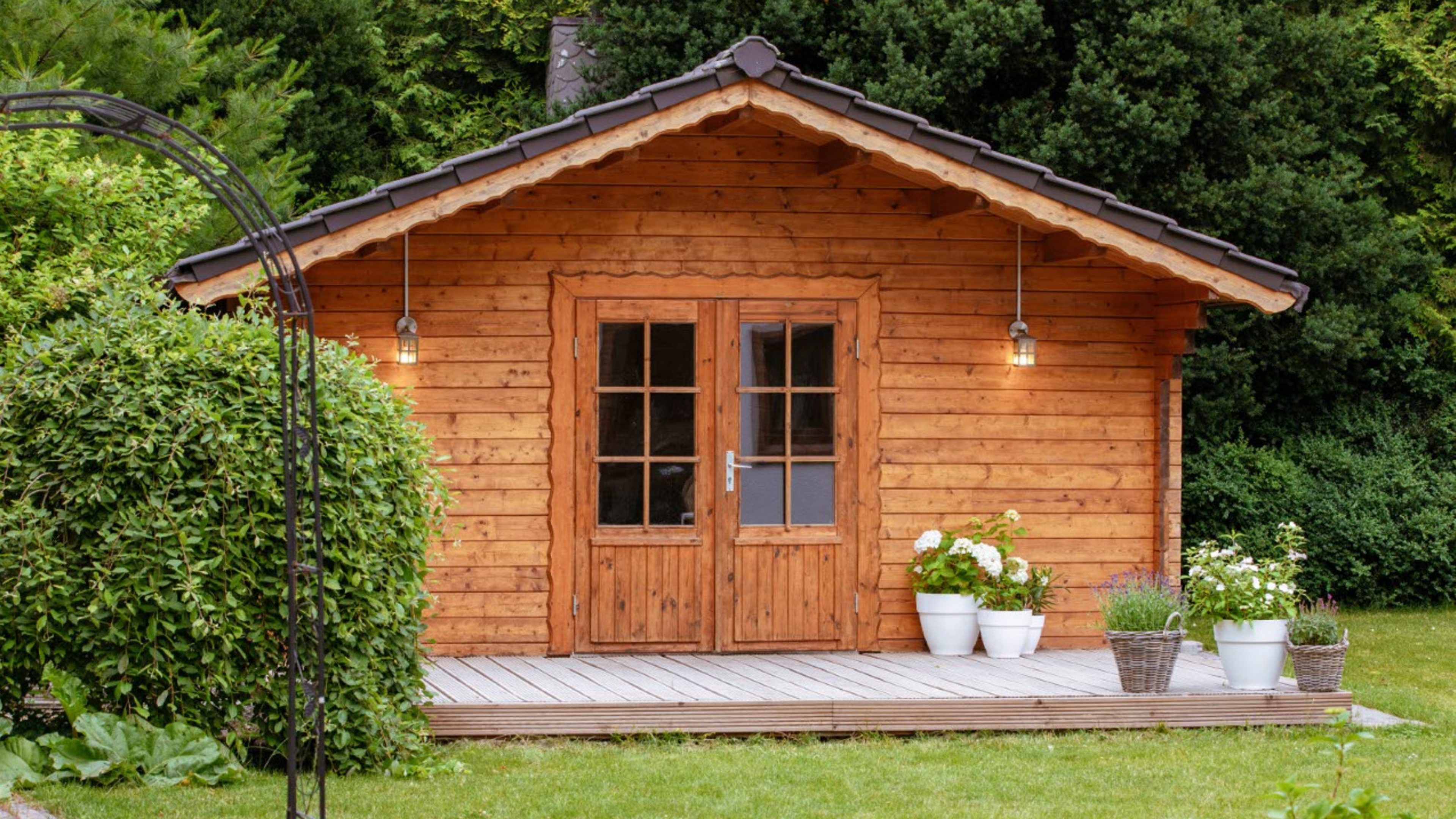 Grosses Gartenhaus aus Holz in einem grünen Garten. Vor dem Gartenhaus hat es viele Töpfe mit Lavendel und Hortensien.