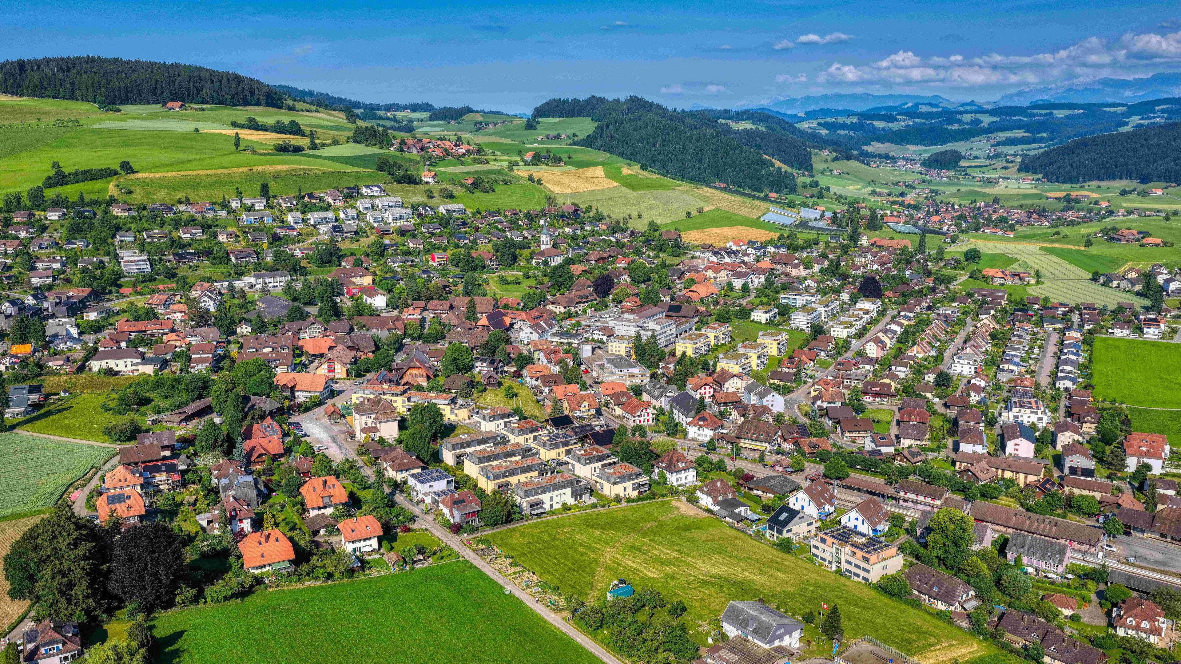 Luftaufnahme von einem Dorf im Kanton Bern: Häuser, grüne Felder, Wälder und blauer Himmel.
