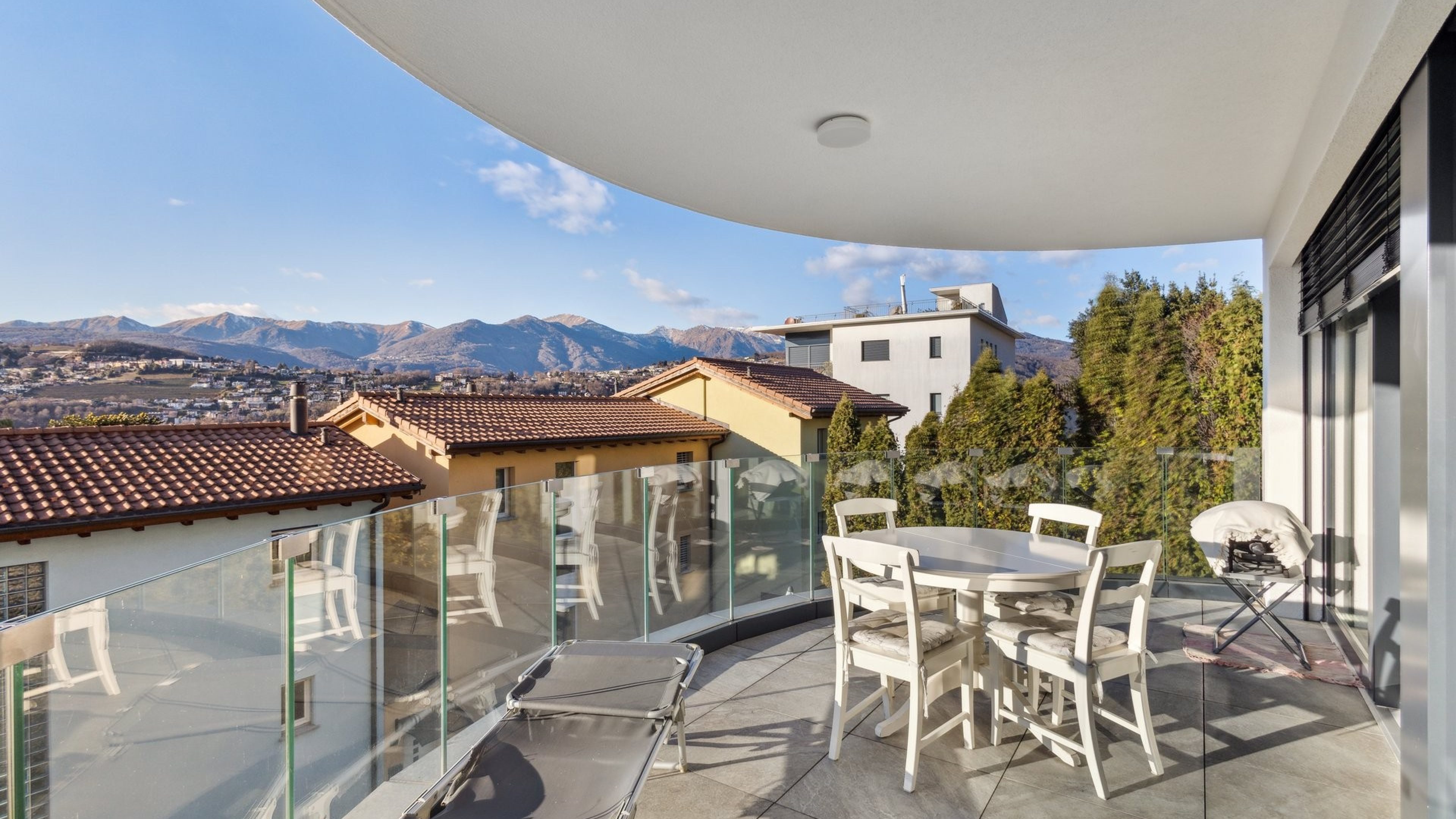Balkon mit Tisch und Stühle, Blick über Dächer und auf die Berge