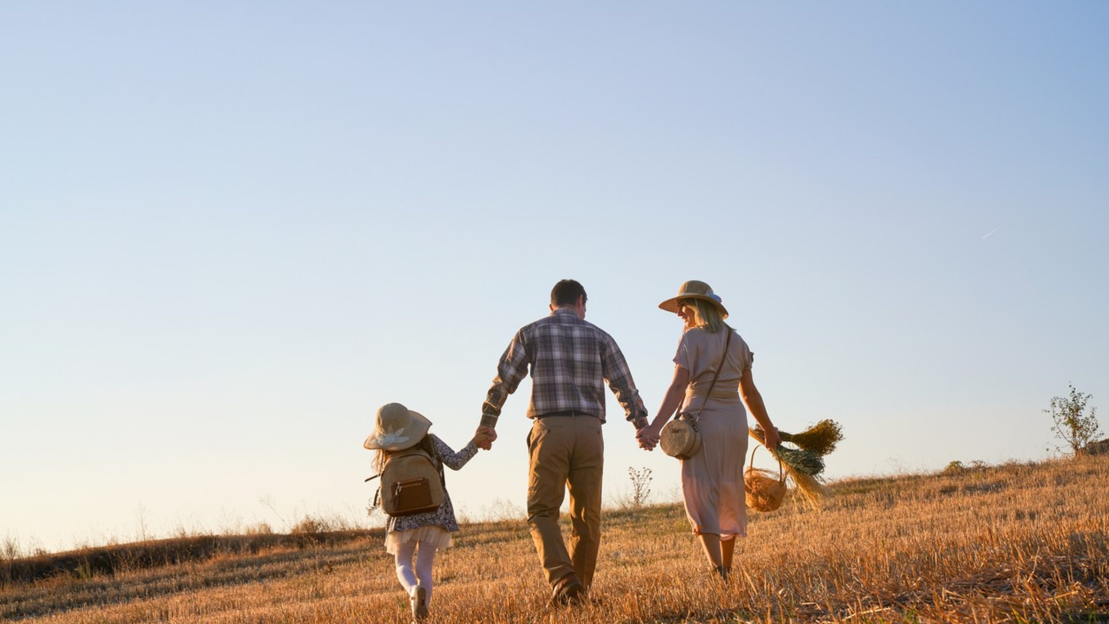 Eltern spazieren mit ihrer Tochter Hand in Hand über ein Feld.