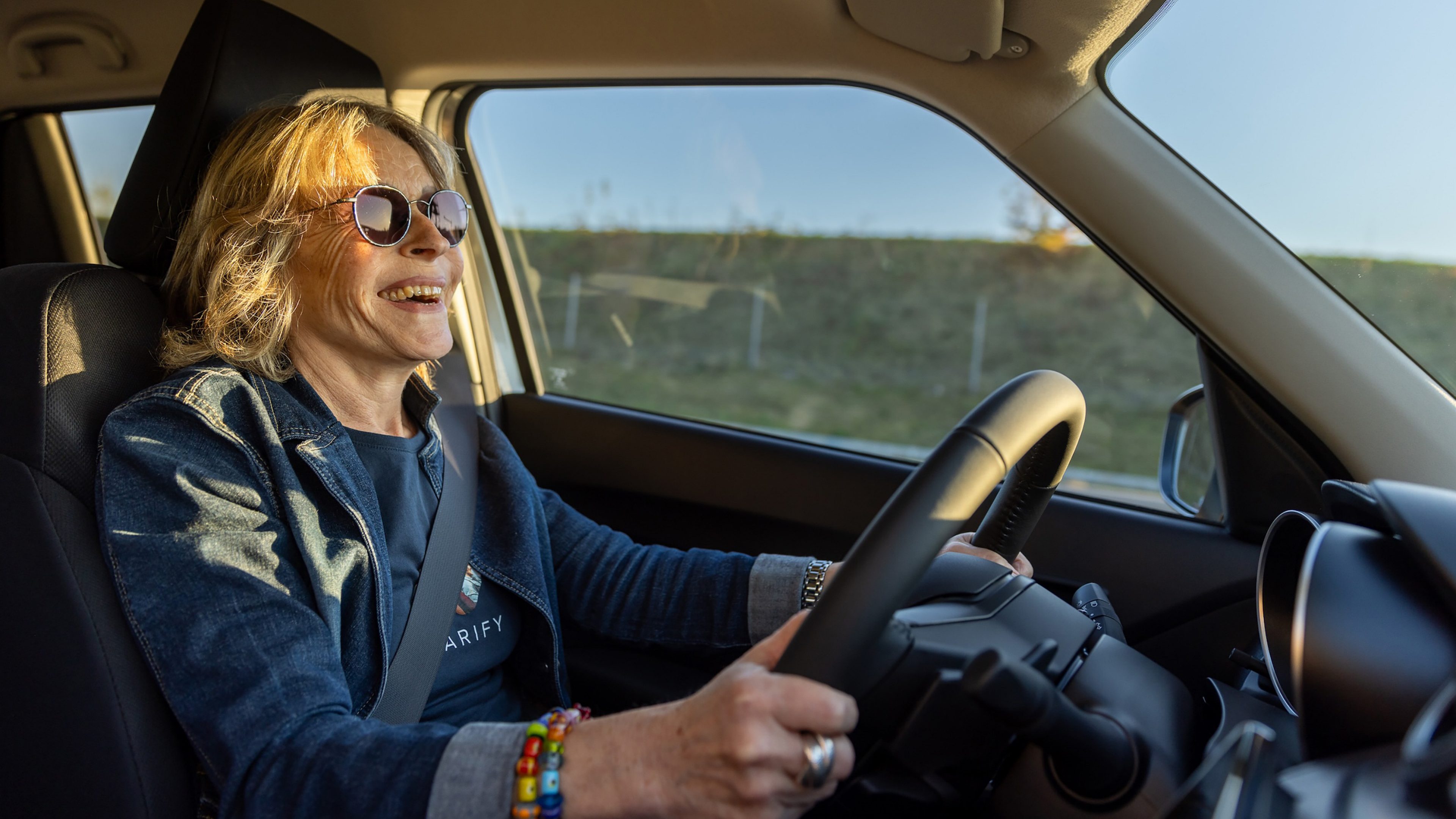 Fotografie Seniorin lachend hinter dem Steuer eines Kleinwagens