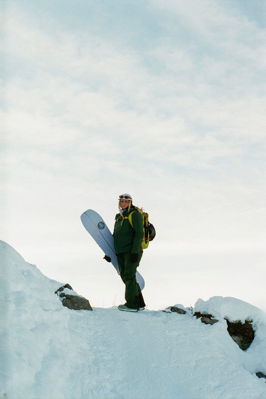 Person hält ein Snowboard in einer sonnigen, verschneiten Berglandschaft – Winter‑Outdoor‑Szene in den Alpen. 