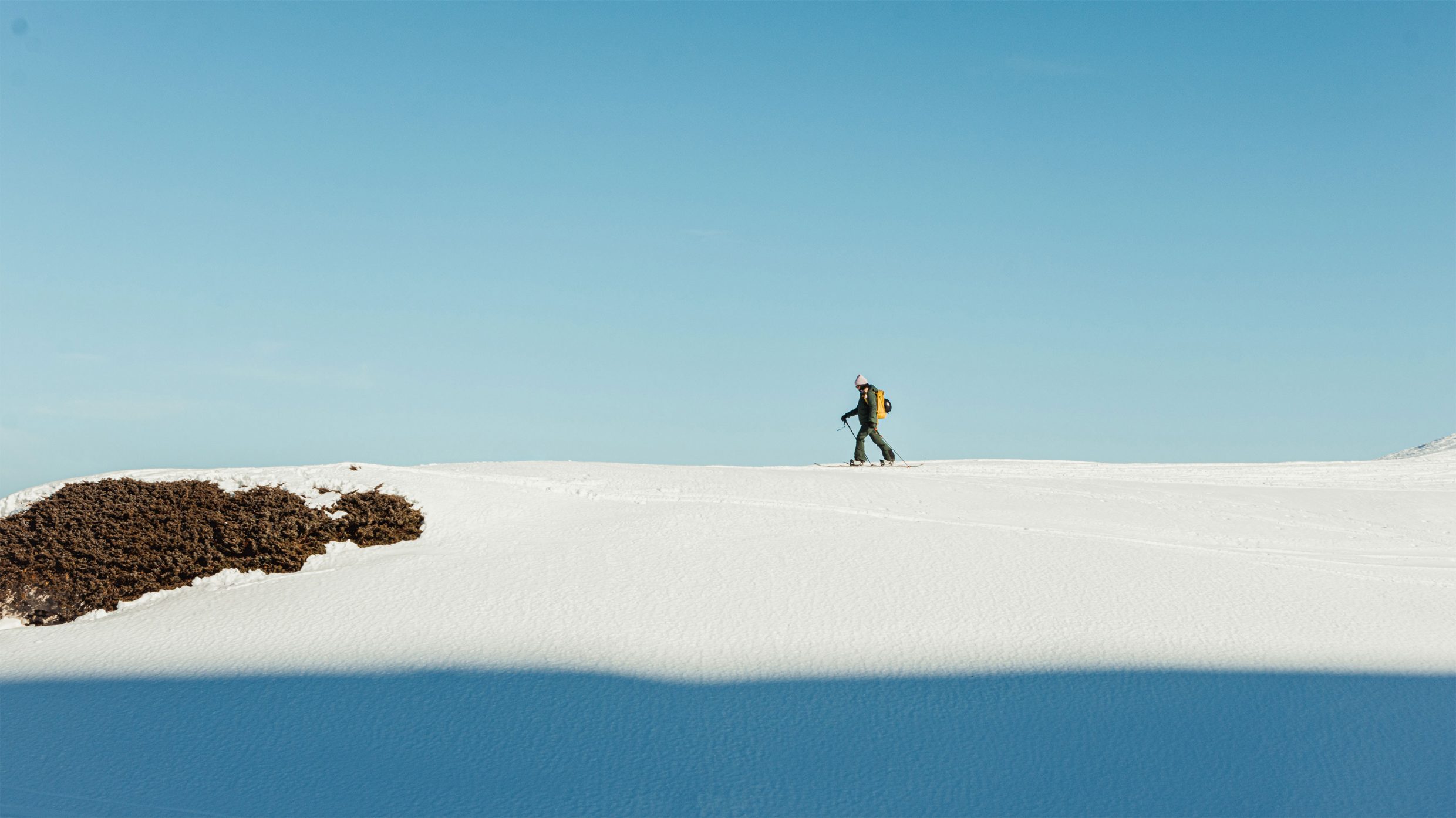 Person auf Skitour wandert über eine unberührte Schneelandschaft unter klarem blauem Himmel.