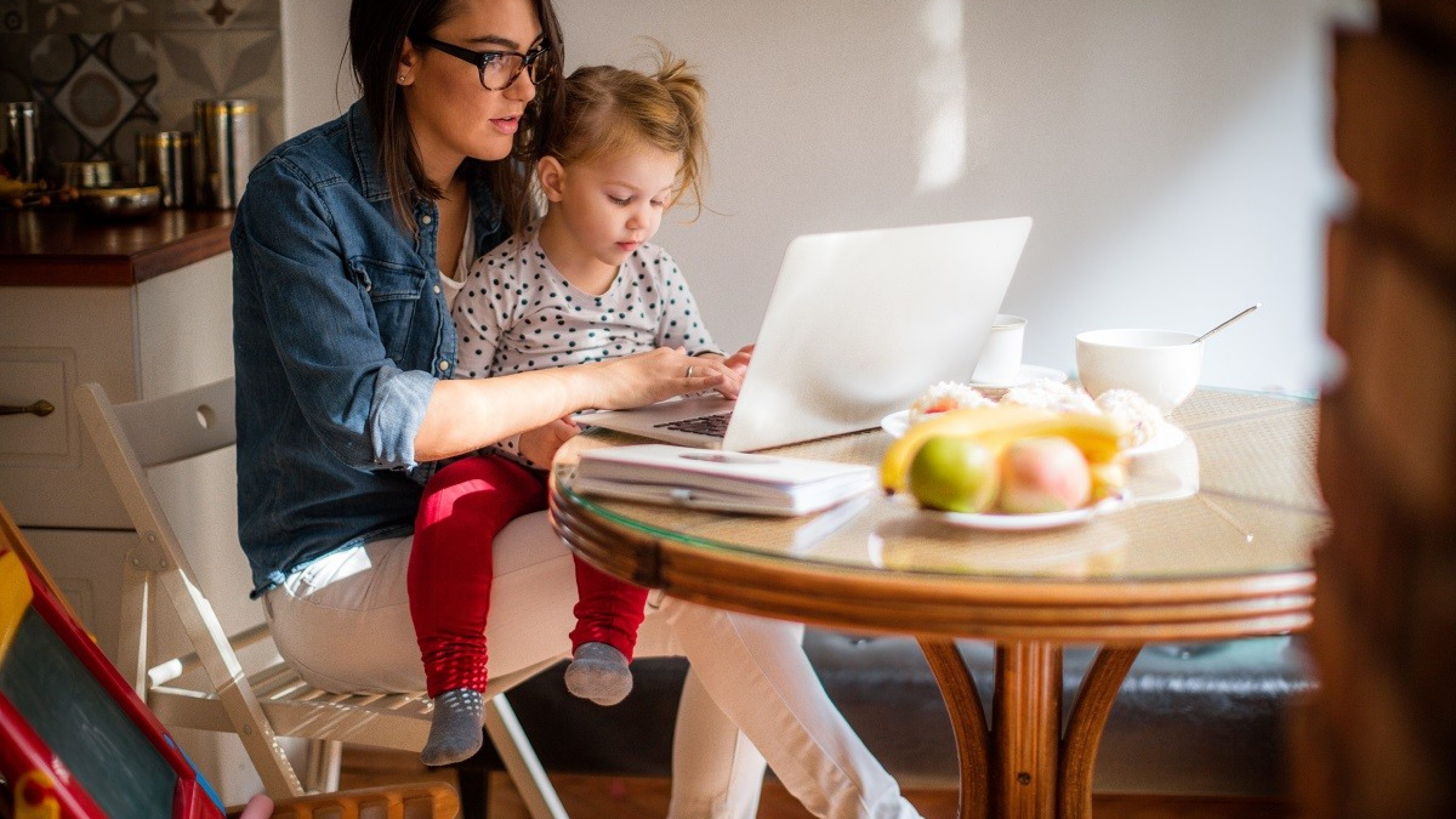 Eine Mutter sitzt mit der kleinen Tochter am Küchentisch und informiert sich am Laptop zur Vorsorge.