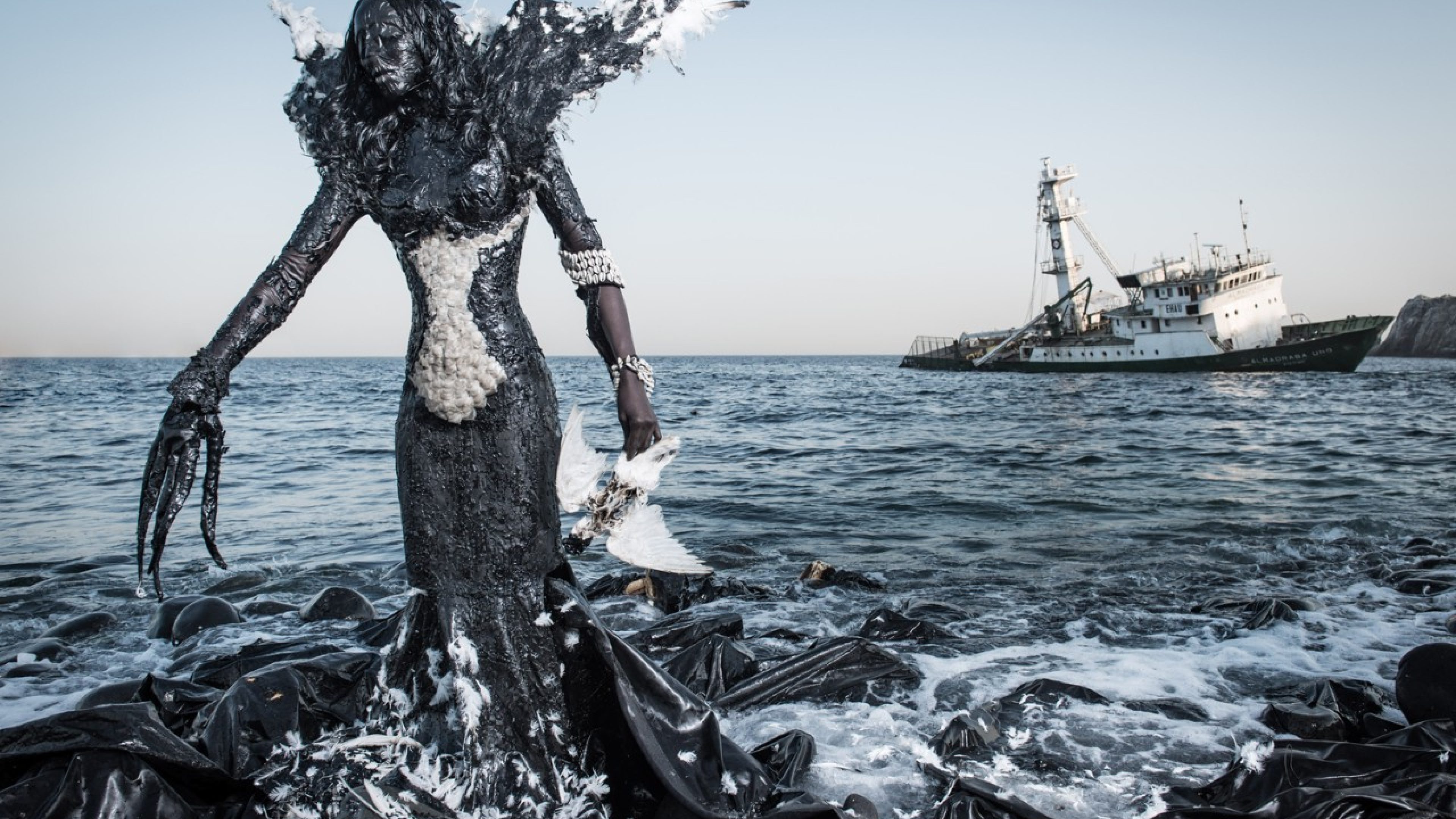 Eine Frau steht in Müll gekleidet im Meer als Symbol für die Verschmutzung der Ozeane.