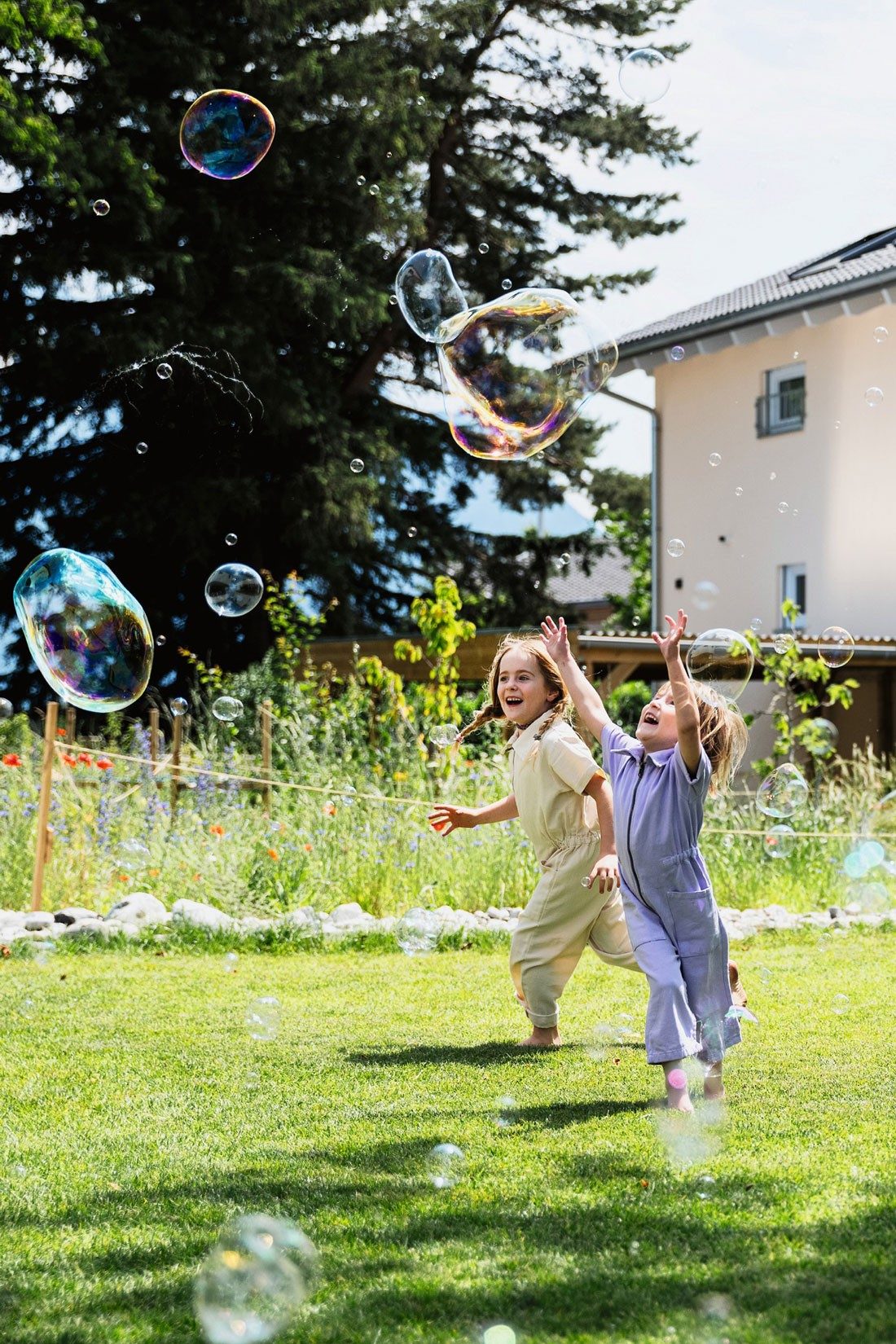 Zwei Kinder spielen in einem Garten mit Seifenblasen.