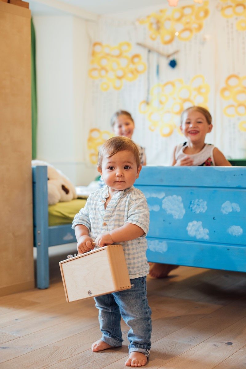Ein Kleinkind mit einem Spielzeug in der Hand steht in einem Kinderzimmer.