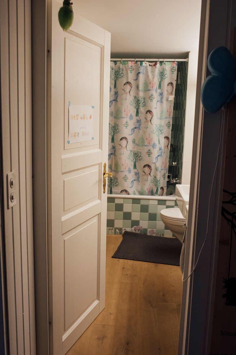 Eine offene Tür, hinter der sich ein Badezimmer mit Badewanne und Duschvorhang verbirgt. 