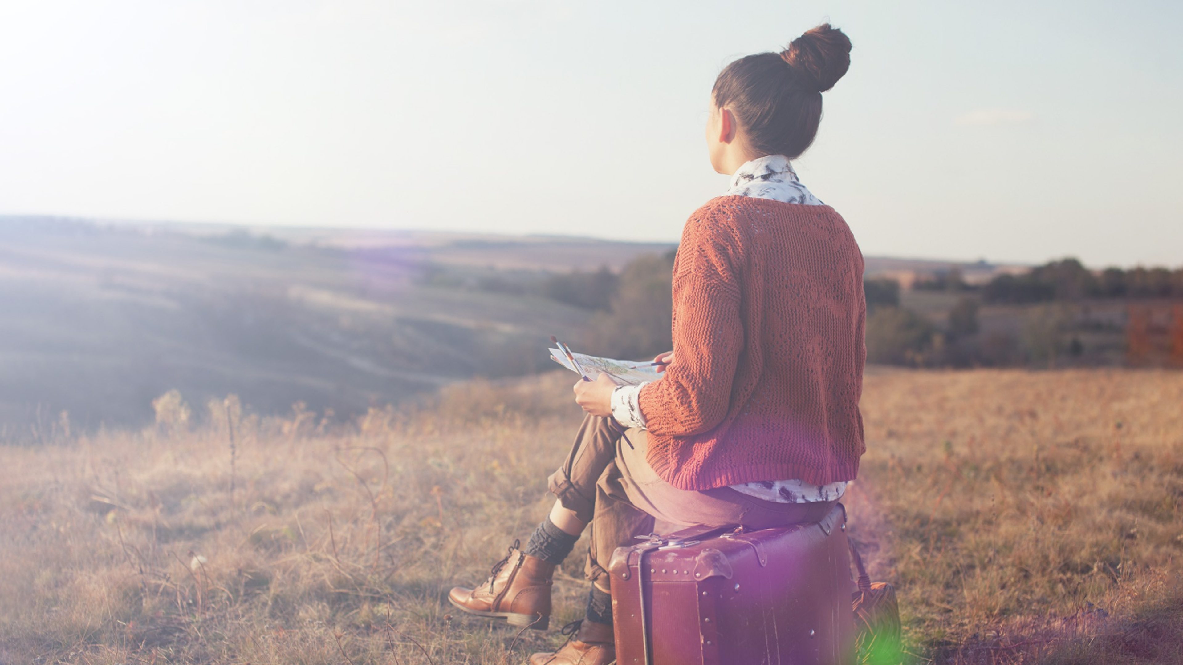 Frau sitzt auf einem Koffer und geniesst den Ausblick in die Natur 