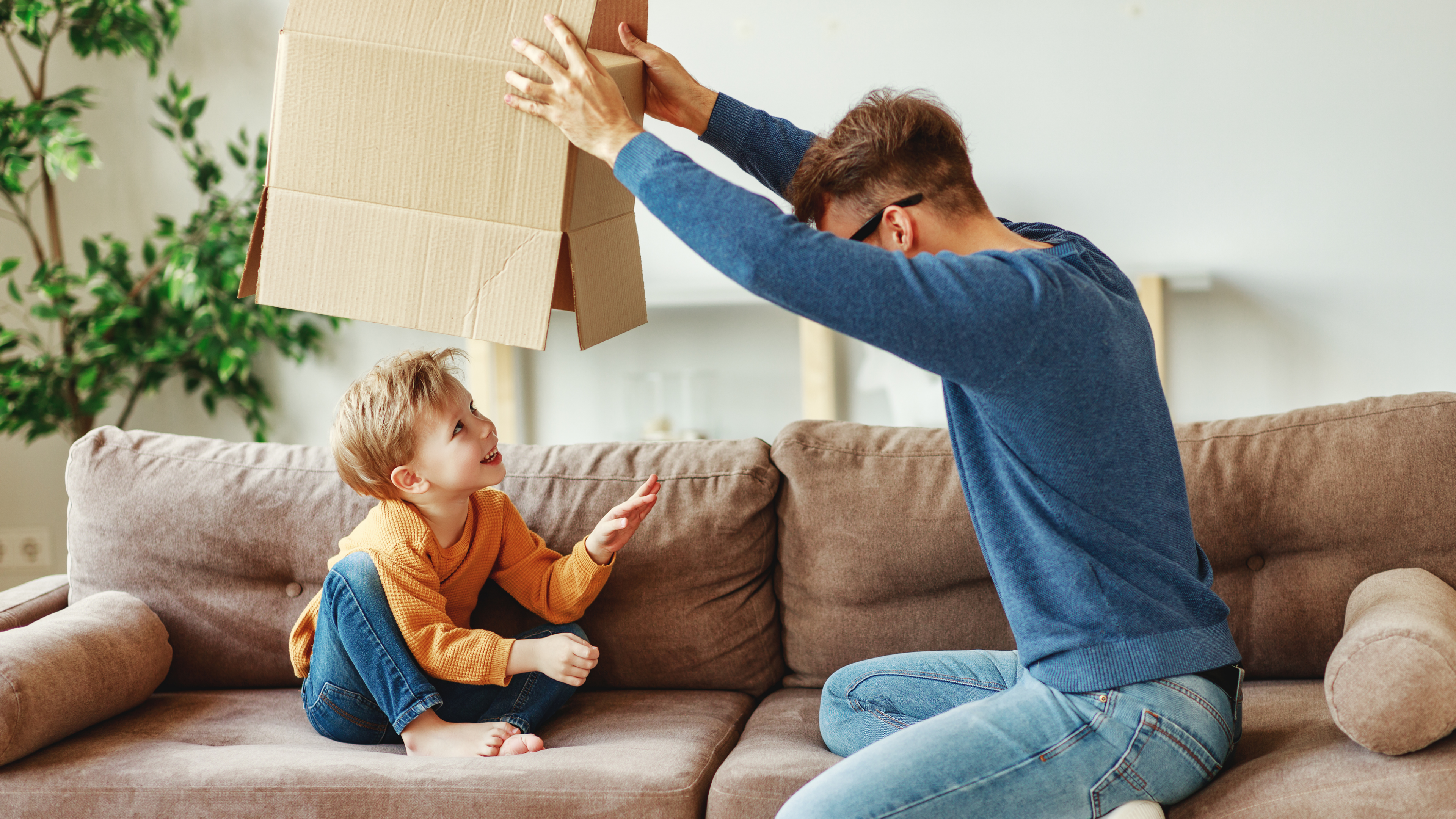 Ein Vater spielt mit seinem Sohn auf dem Sofa des Eigenheims.