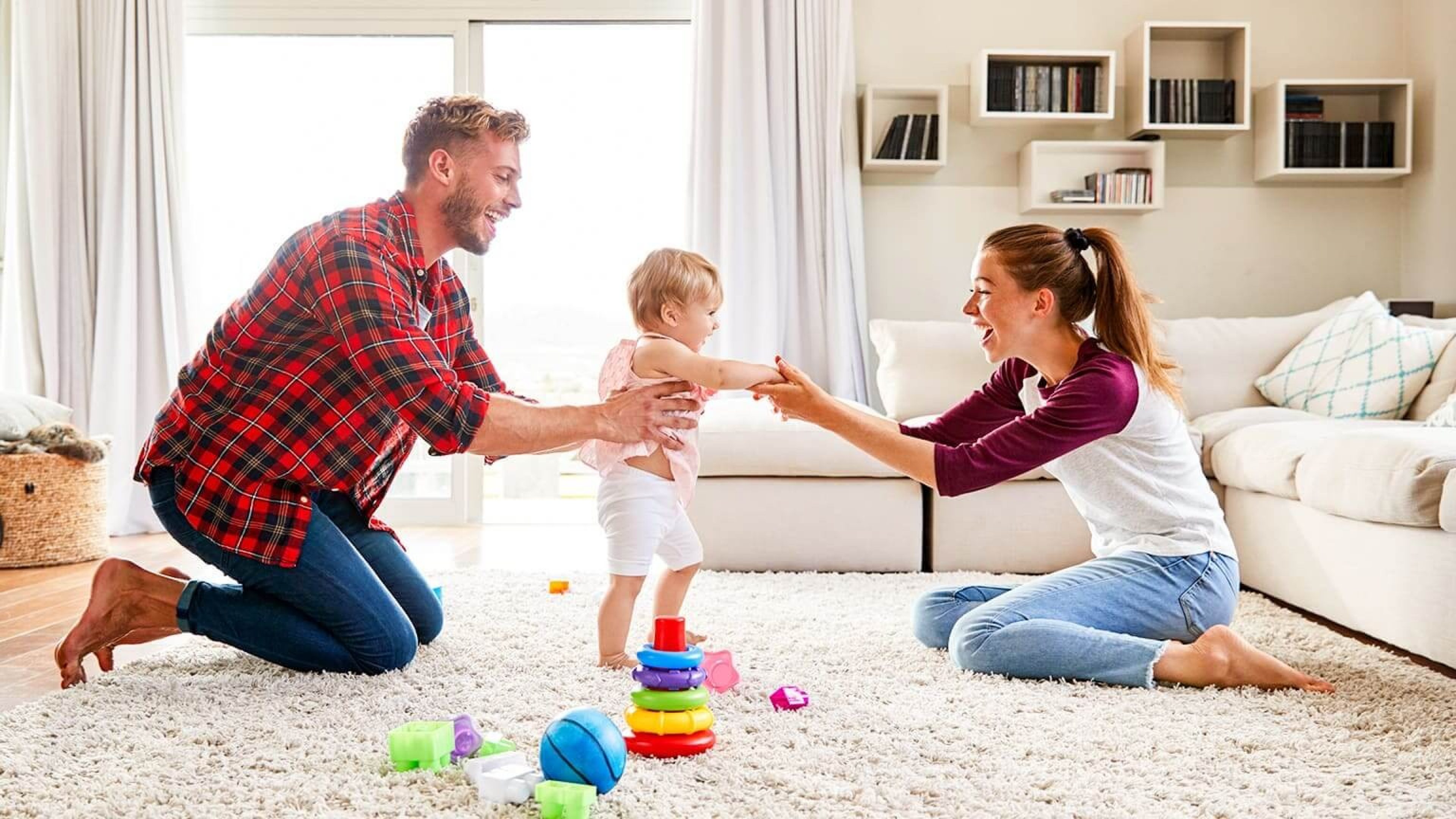 Eltern spielen mit Kleinkind im Wohnzimmer des Eigenheims.