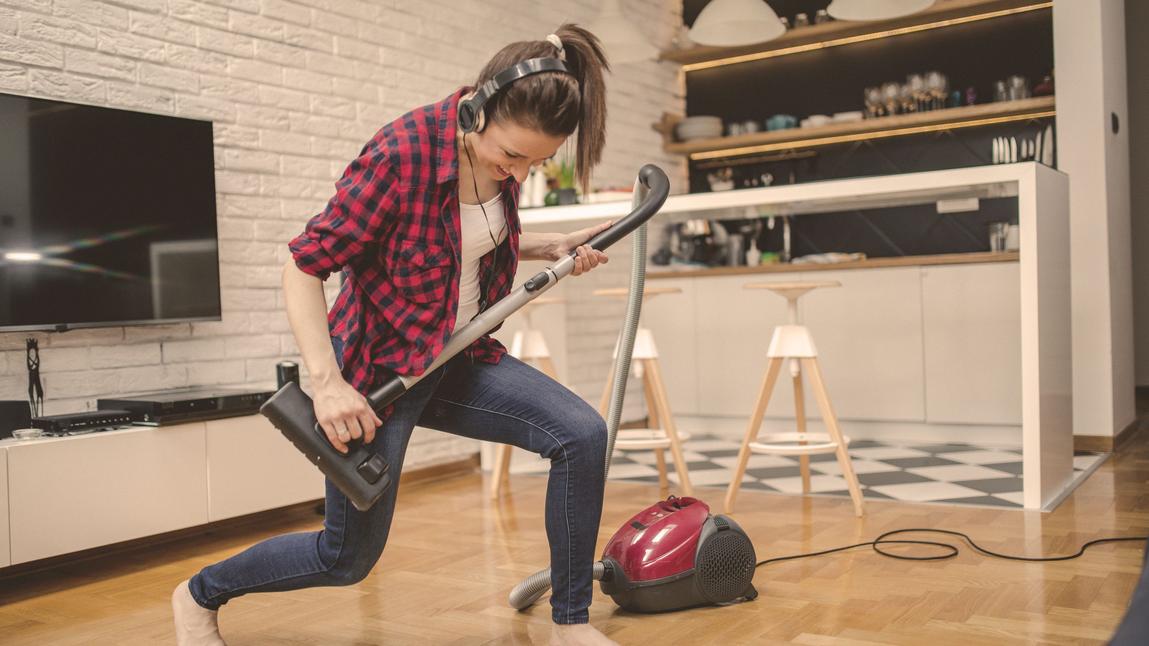 Eine junge Frau spielt Luftgitarre mit dem Staubsauger.