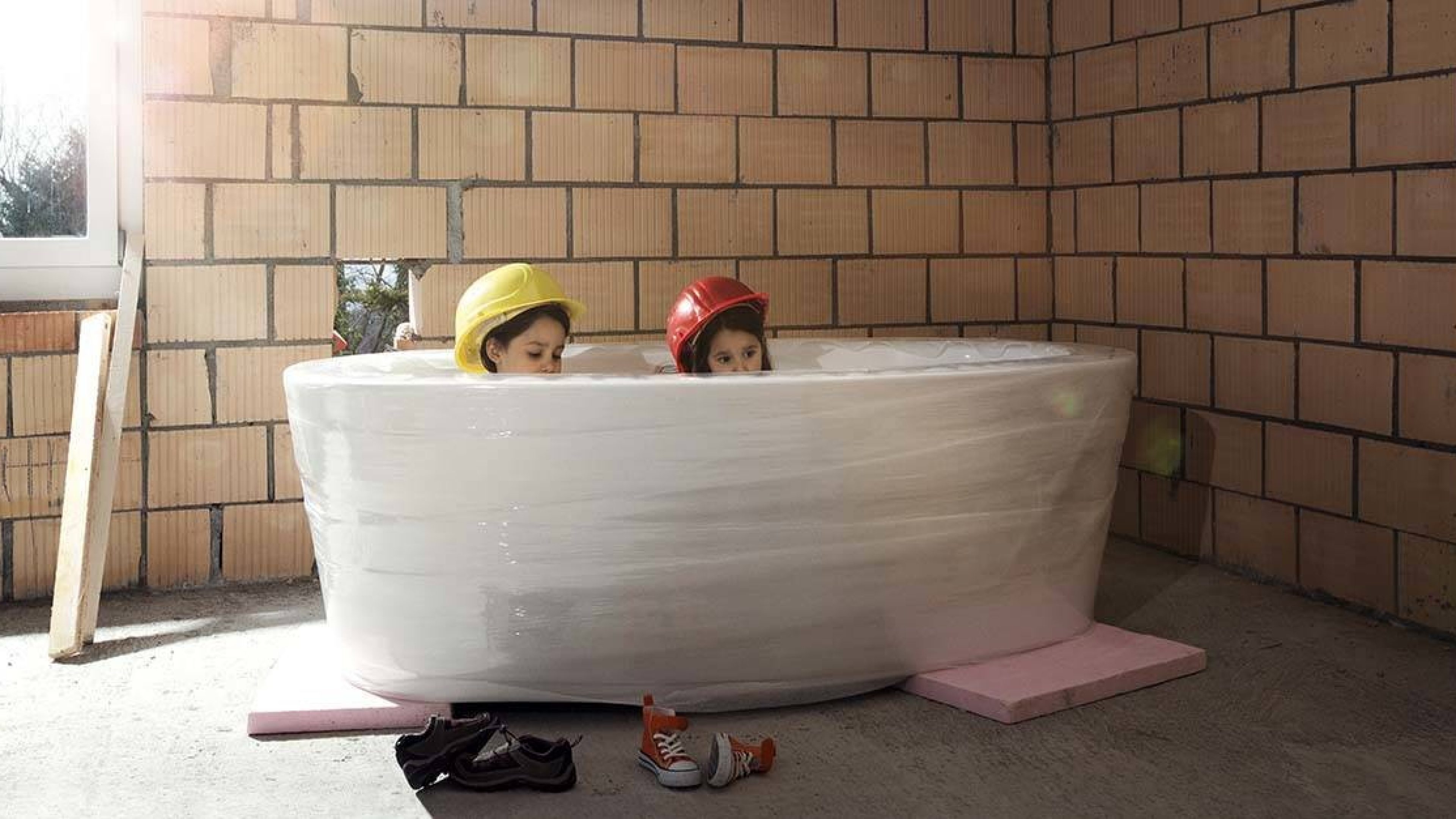 Kinder sitzen in Badewanne im Rohbau des Eigenheims