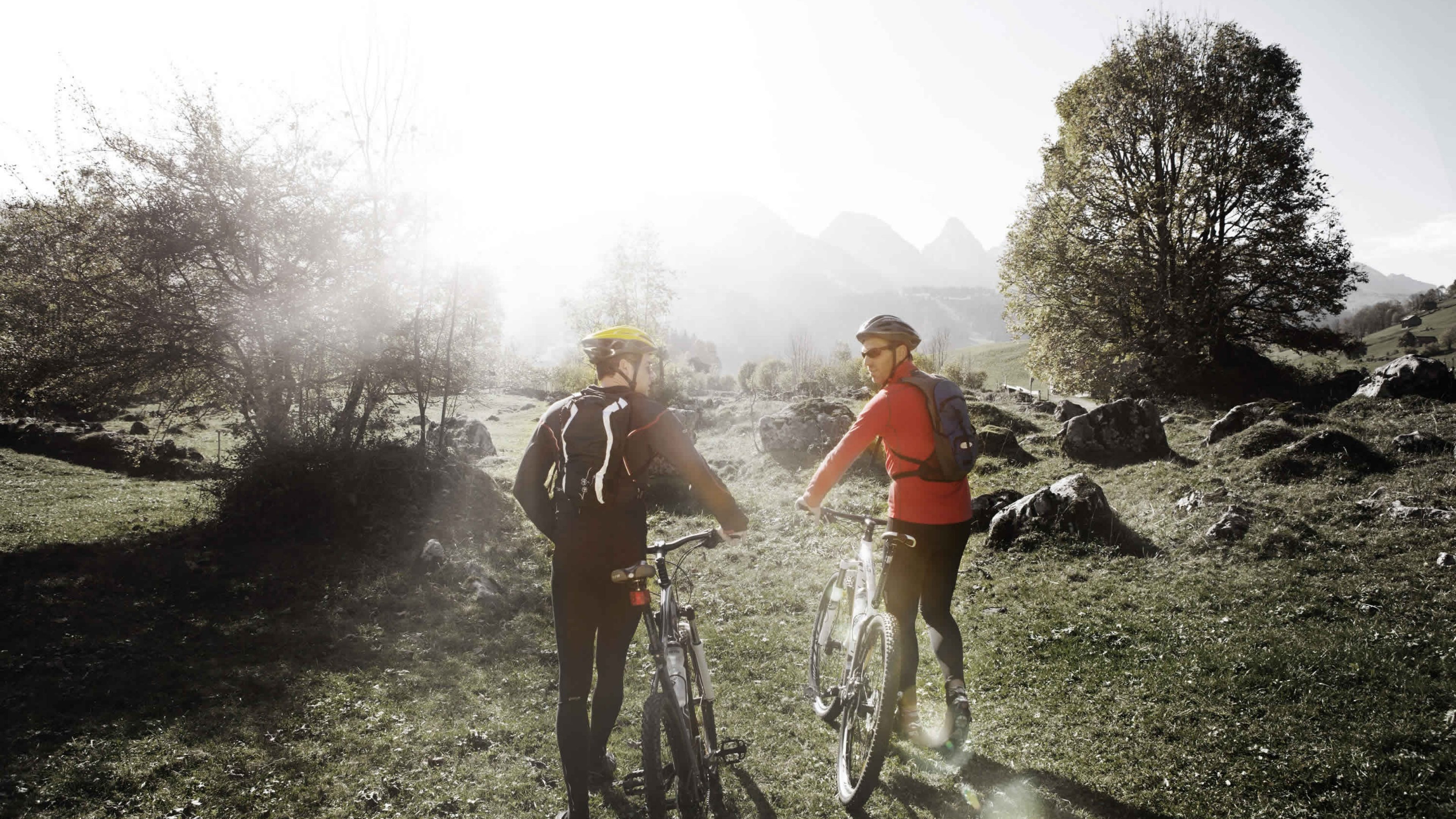 Zwei Sportler sind mit ihren Bikes unterwegs in den Bergen.