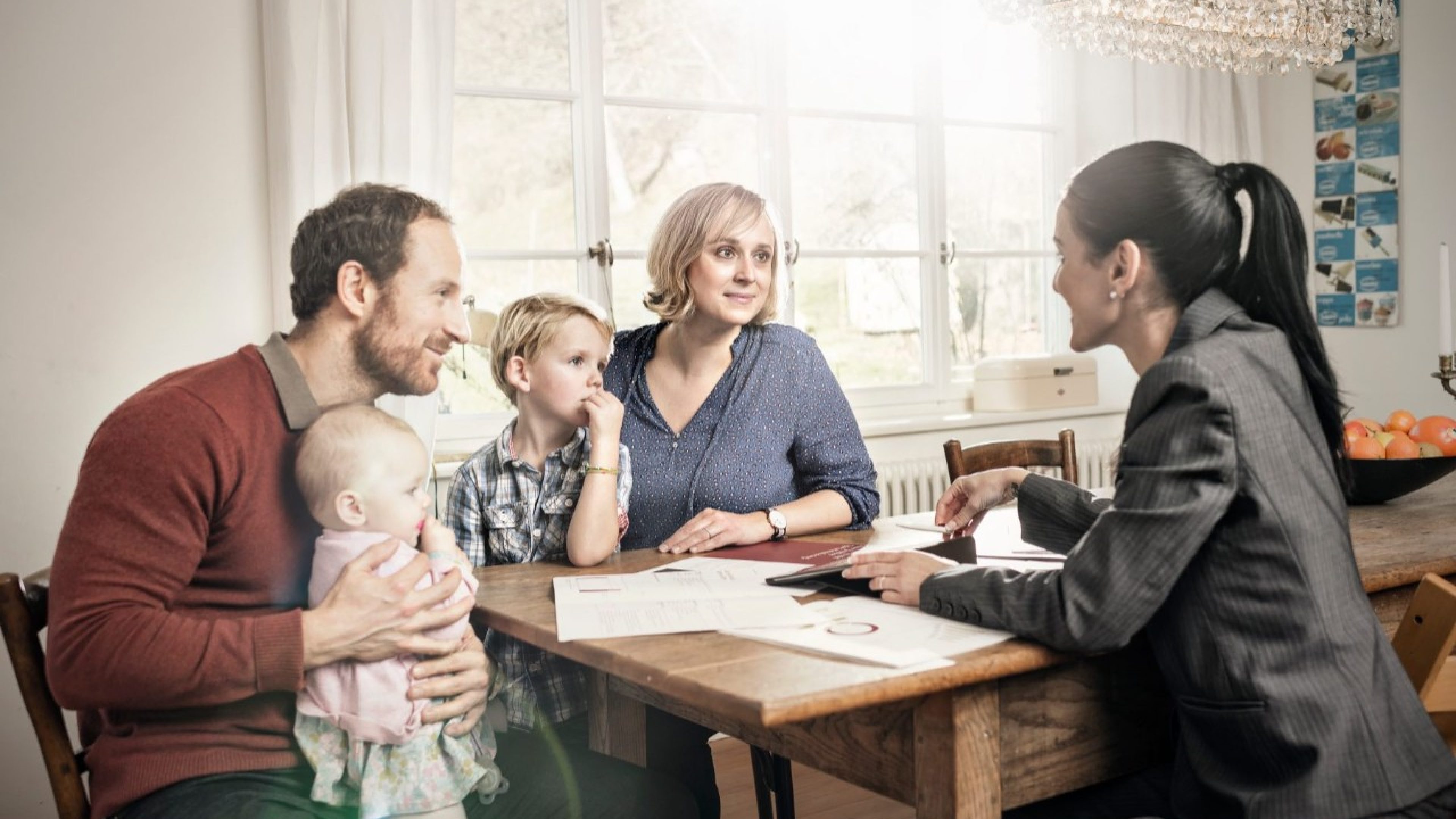 Eltern und zwei Kinder sitzen mit Beraterin am Küchentisch und besprechen Risikodeckung.
