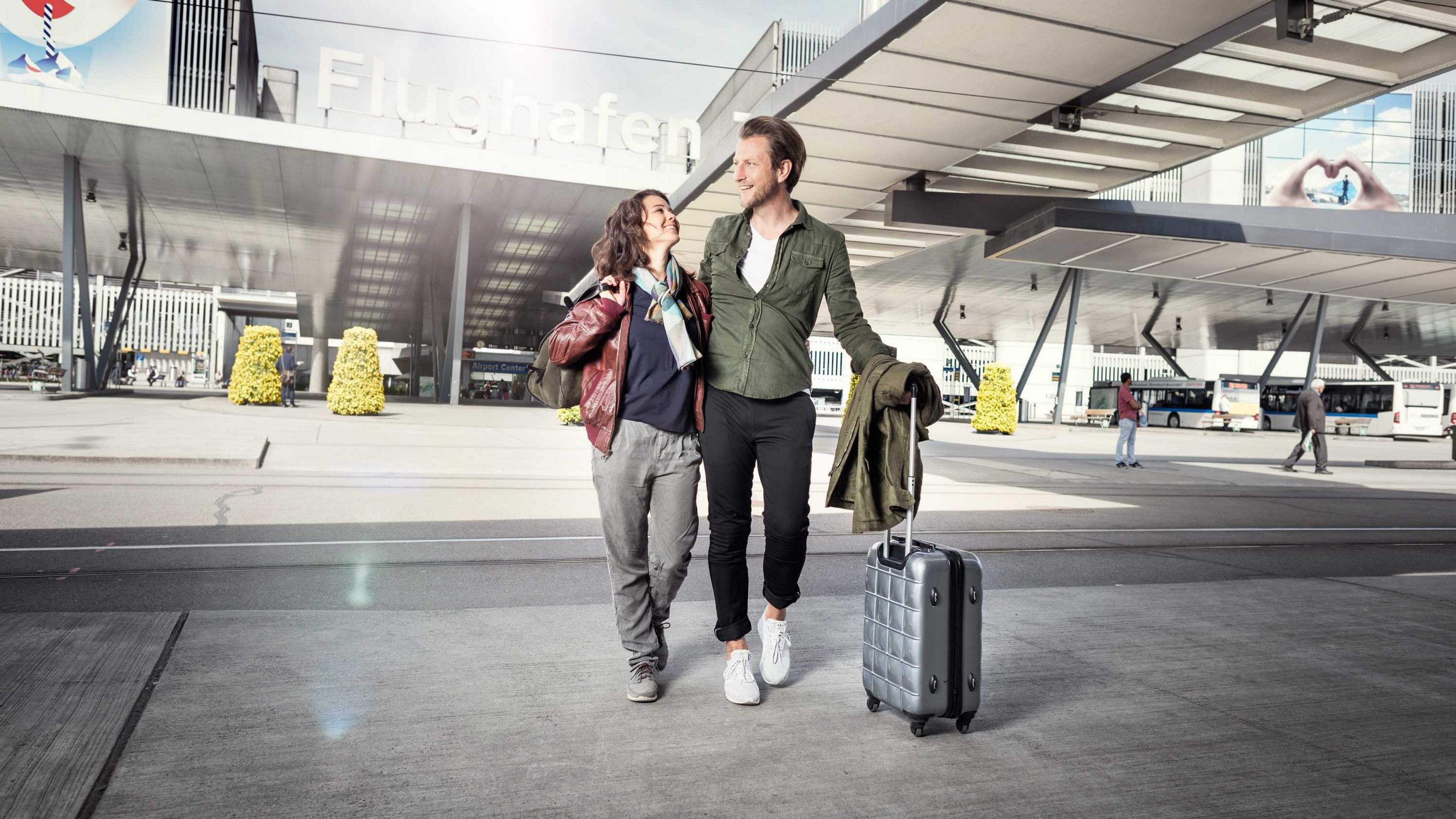 Paar verlässt Flughafen mit Koffer und bespricht Vorsorgethemen.