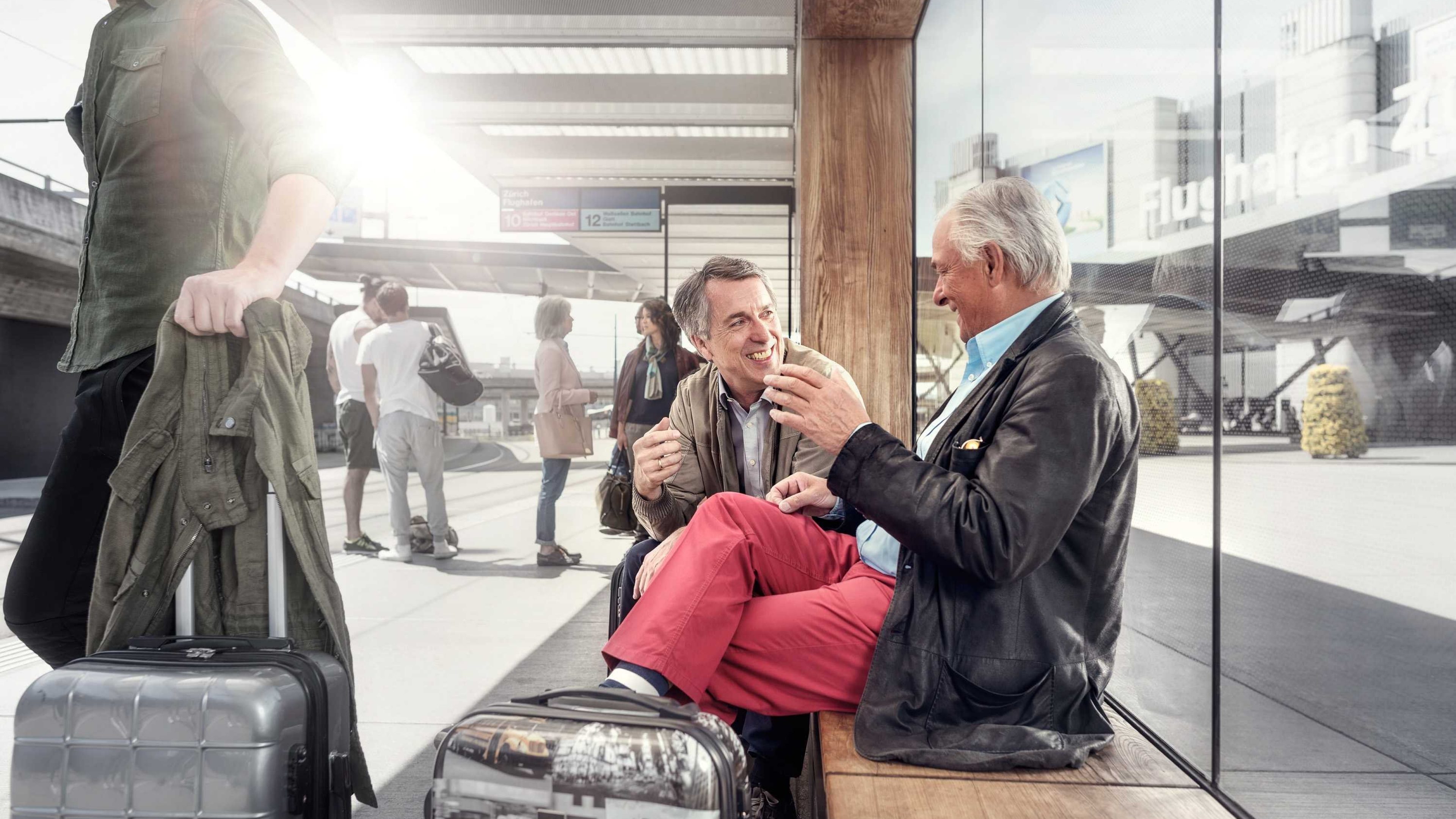 Ein Vater sitzt mit seinem Sohn auf einer Wartebank mit gepackten Koffern, bereit sich zum Auswandern beraten zu lassen. 