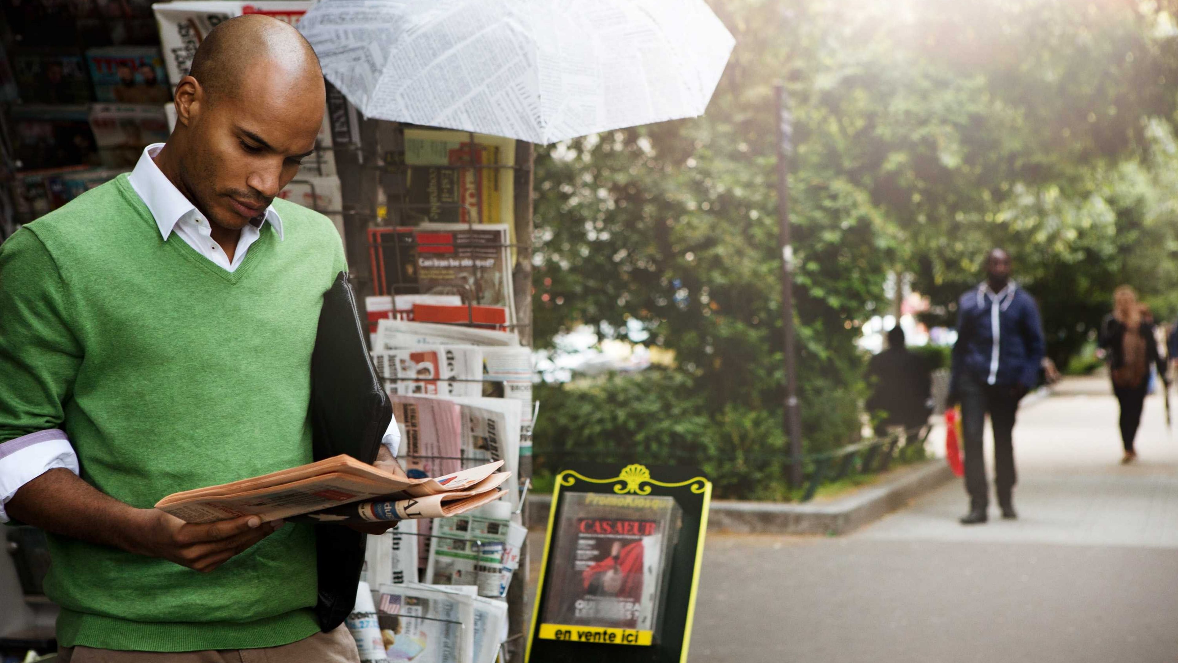 Ein Mann steht vor dem Kiosk und liest die Zeitung.