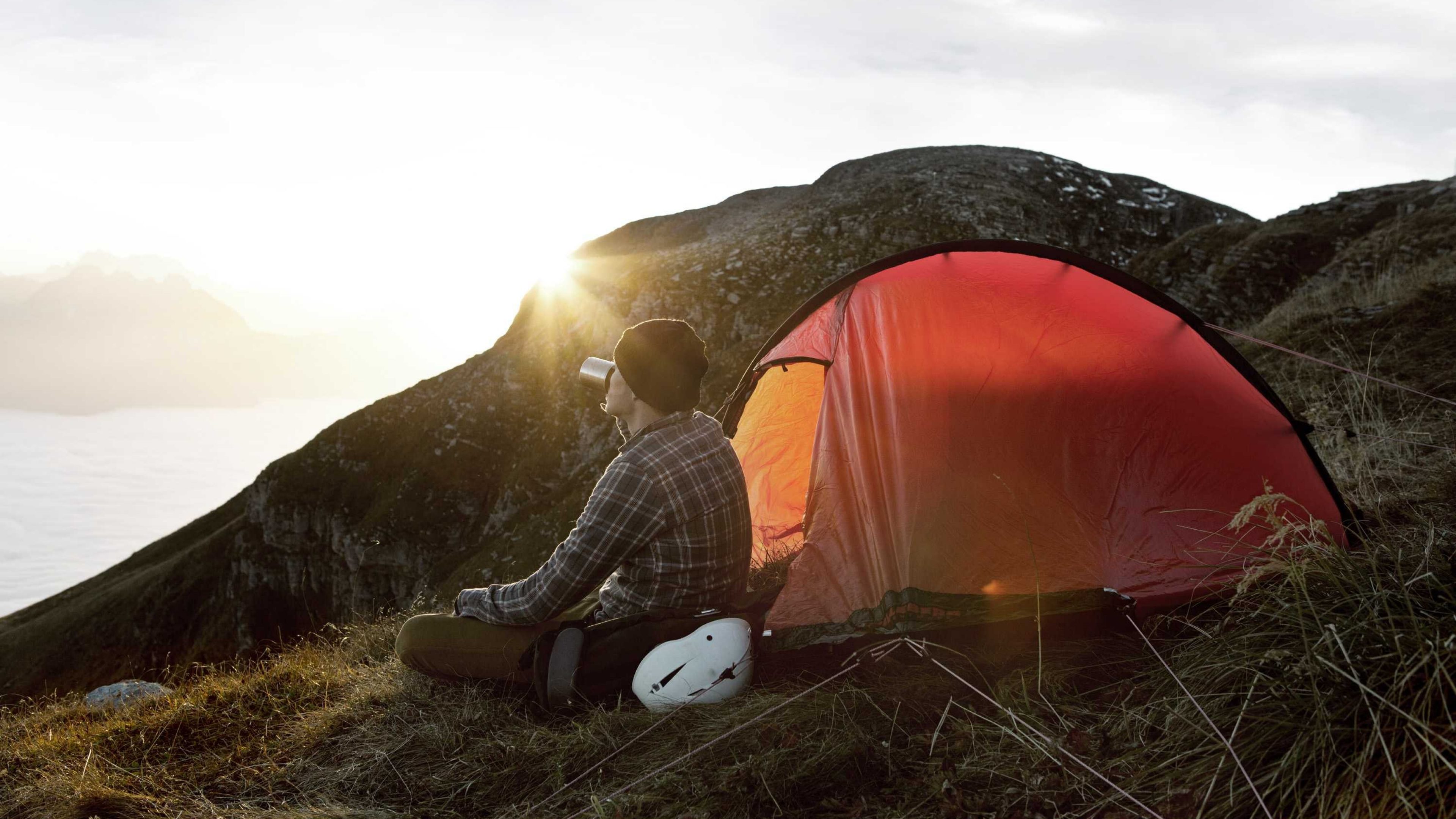 Ein Wanderer sitzt auf einem Berggipfel vor seinem Zelt.
