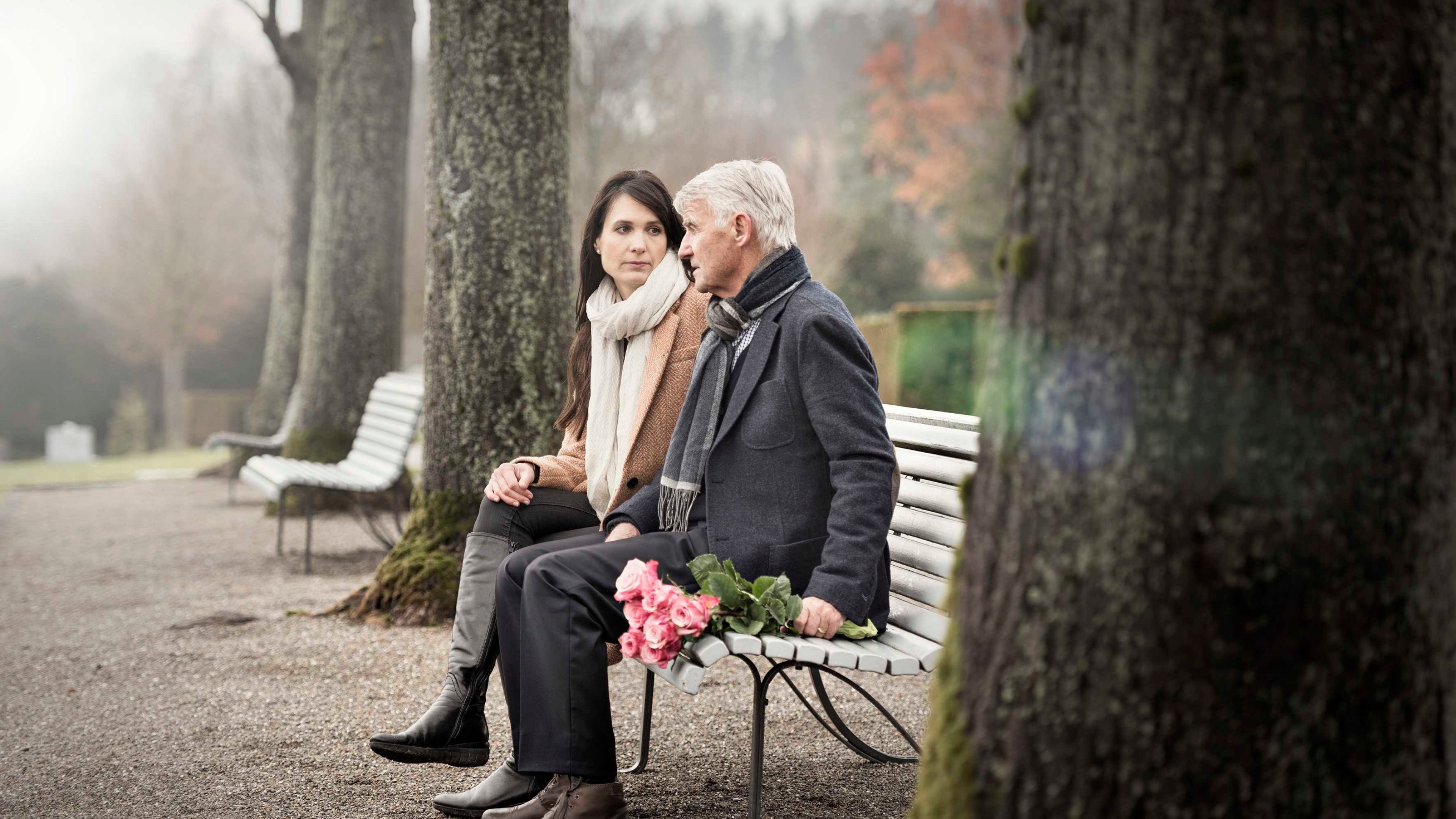 Vater und Tochter sitzen auf einer Parkbank auf dem Friedhof.