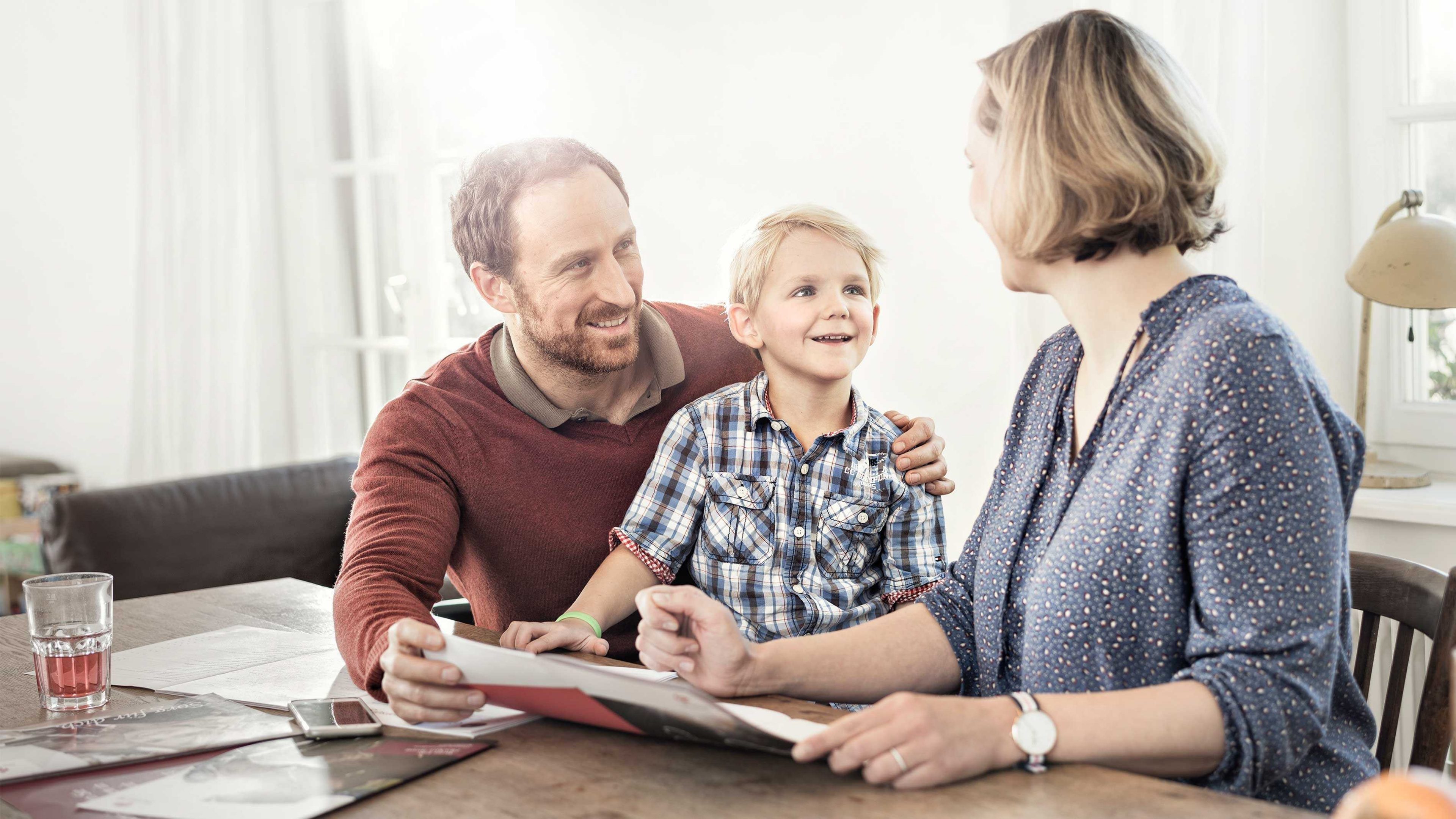 Eltern sitzen mit Kind am Tisch und besprechen Budgetplanung