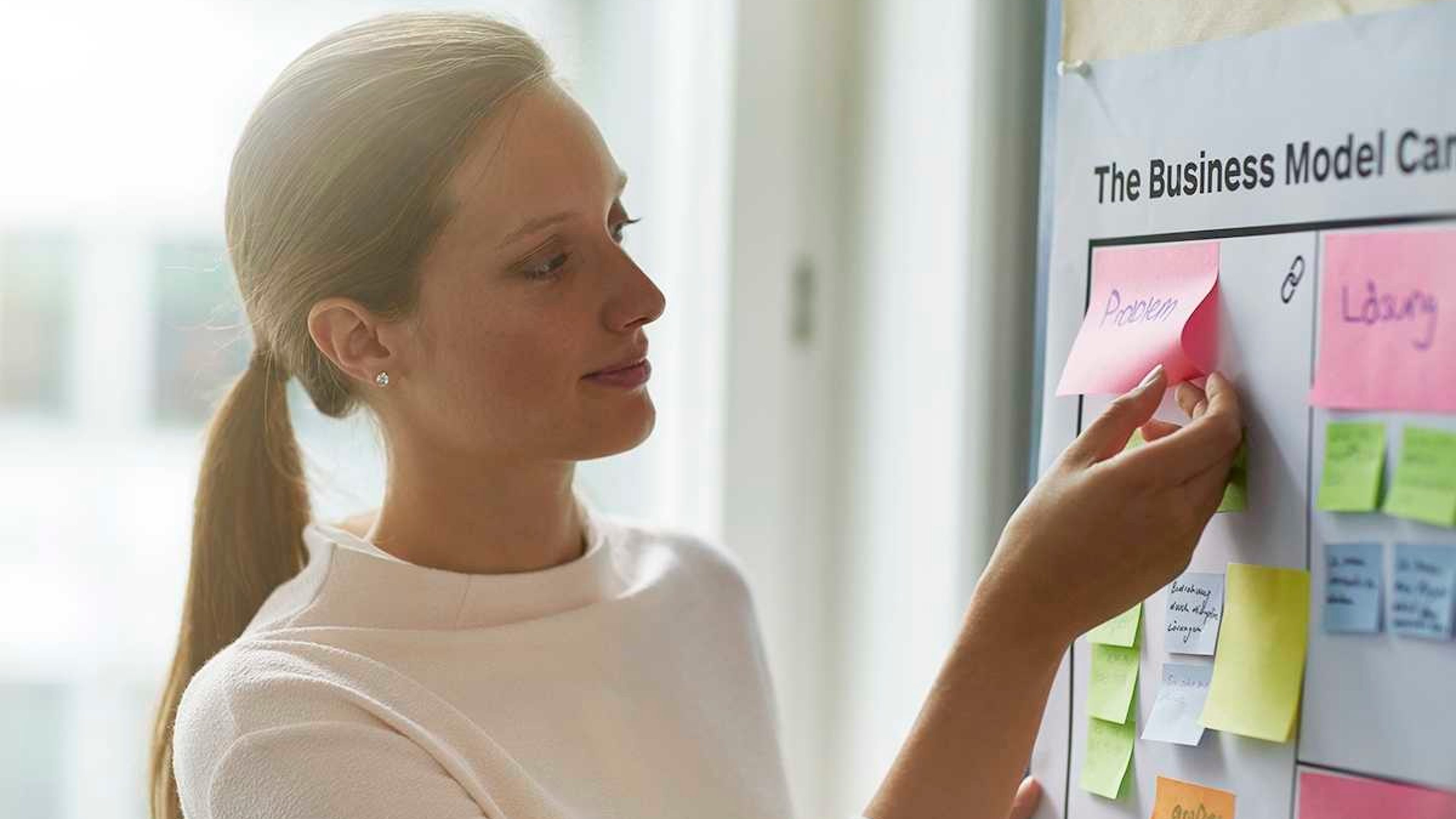 Junge Frau hängt Notizen zum Thema Selbständigkeit an der Wand auf.