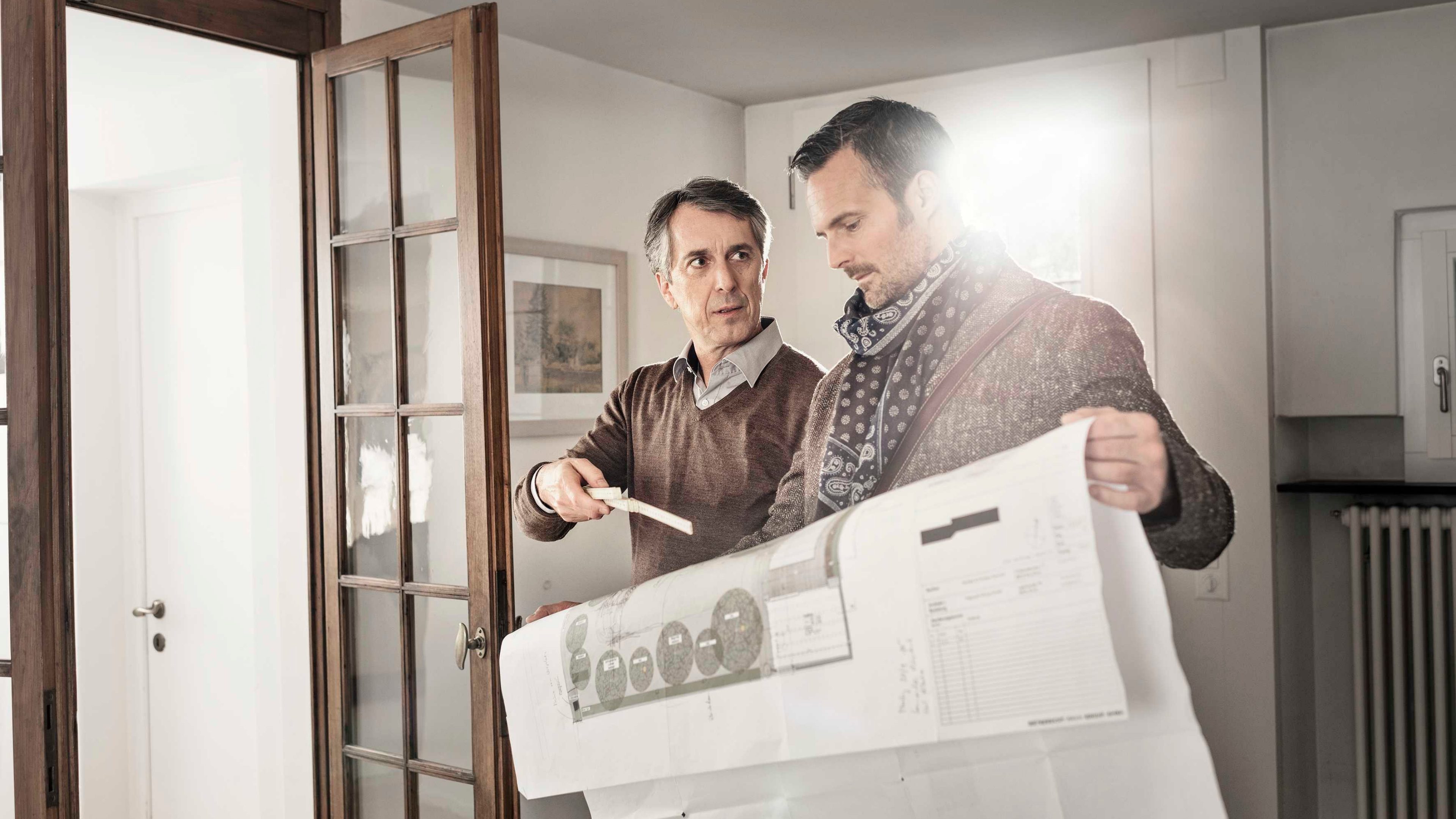 Vater und Sohn stehen in einem Zimmer und besprechen ein Anlagedokument.