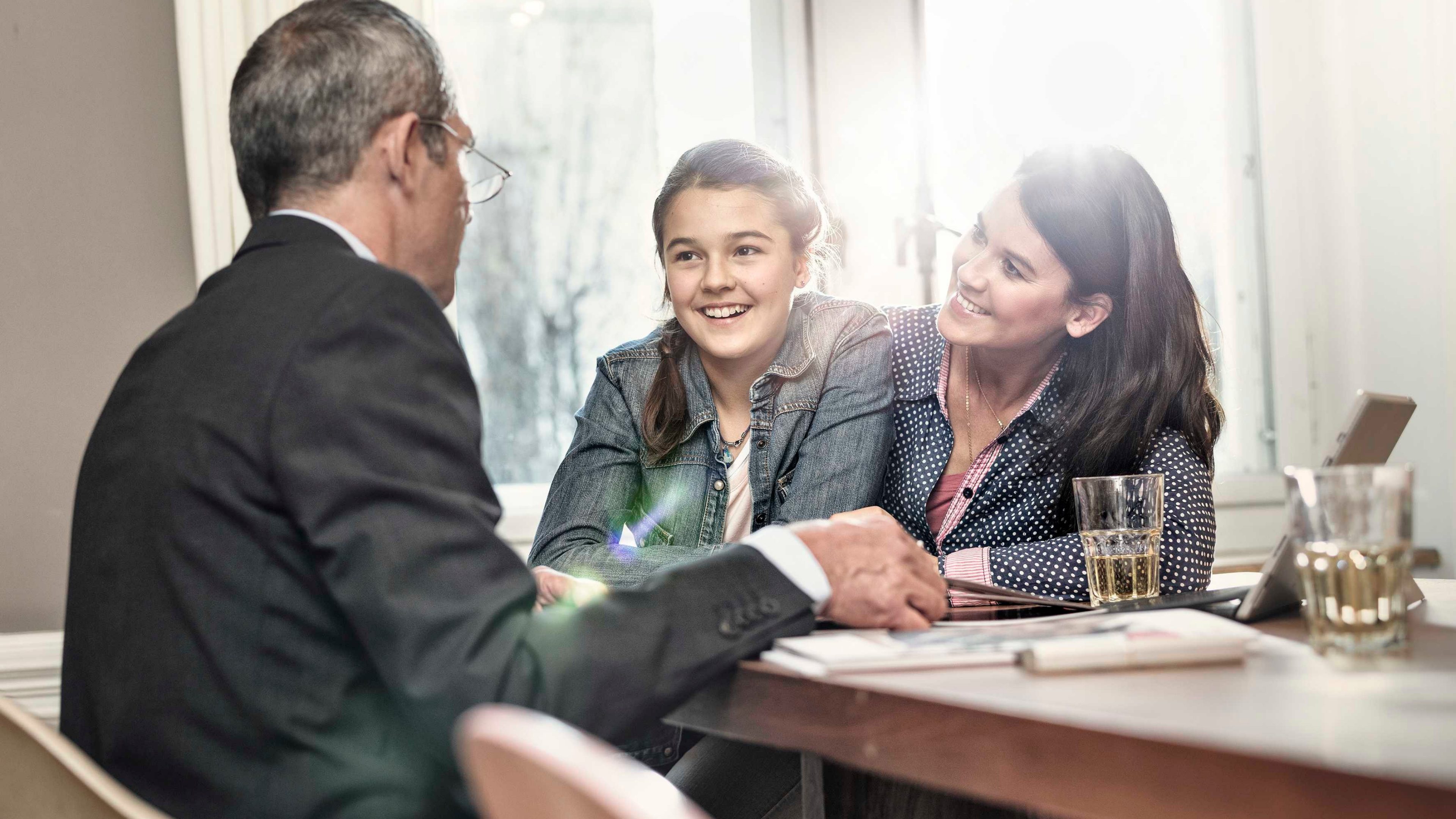 Mutter und Tochter besprechen zuhause Sparversicherungen mit einem Berater.