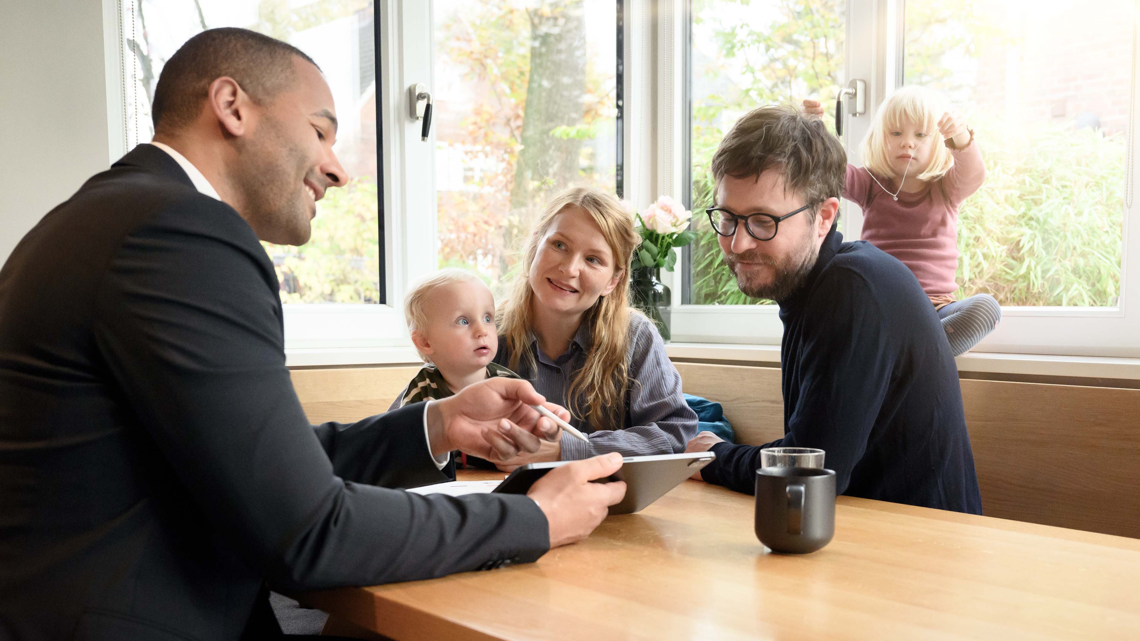 Eltern mit zwei Kindern sitzen mit Berater am Tisch.