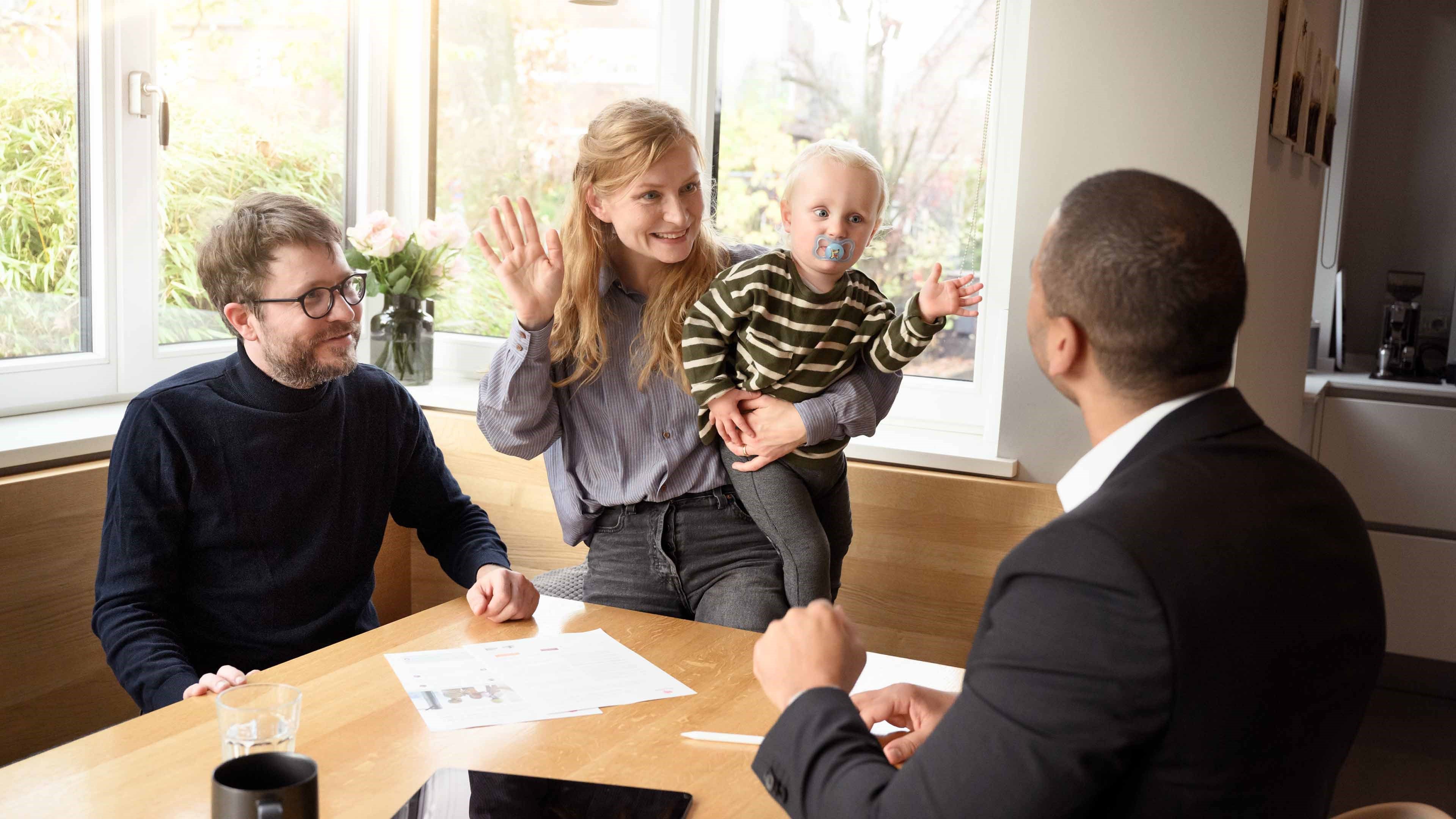 Eltern und zwei Kinder sitzen mit Beraterin am Küchentisch und besprechen Risikodeckung.