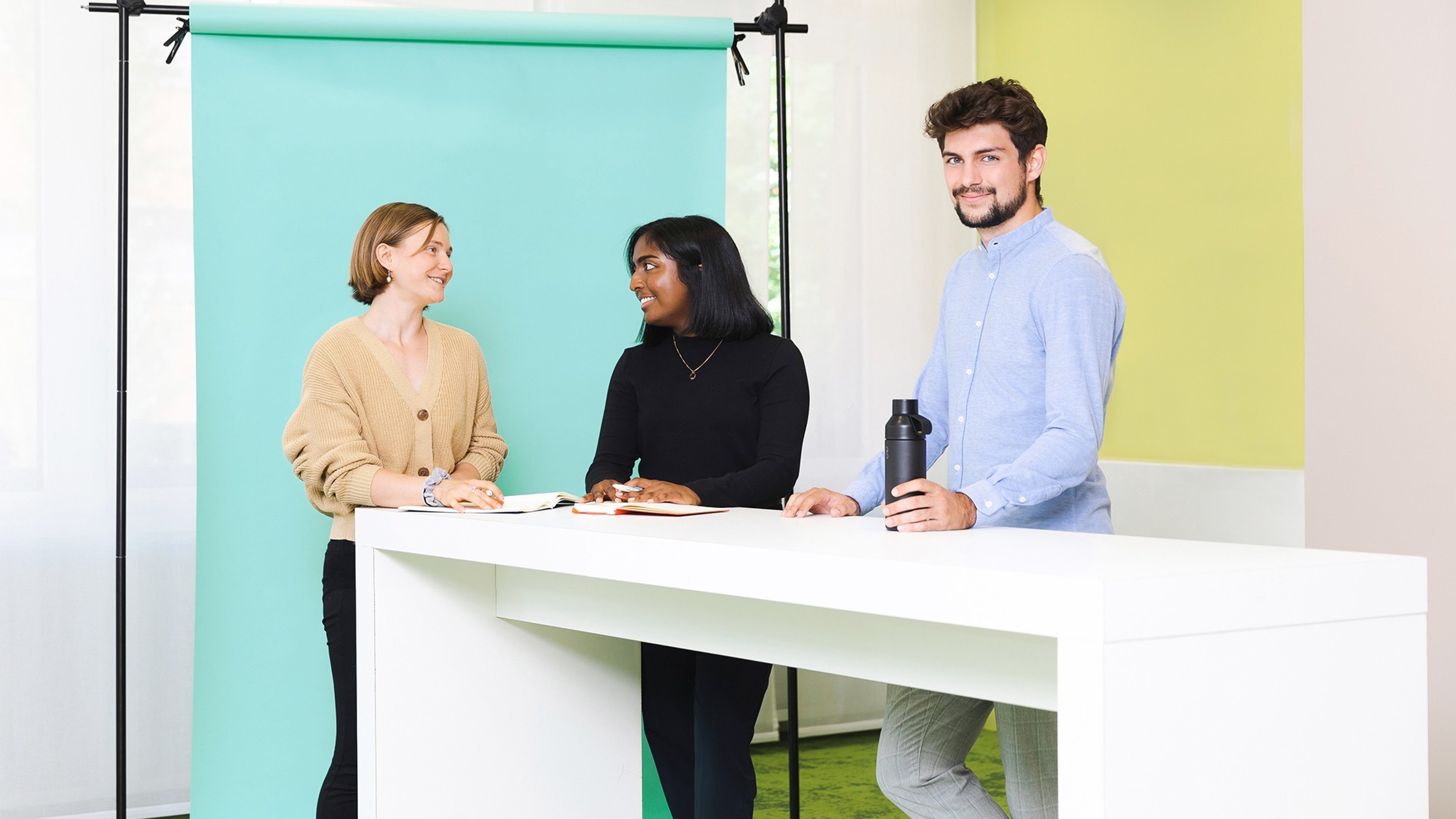 Drei Future Minds stehen gemeinsam an einem Stehtisch, die zwei Frauen unterhalten sich, der Mann, der ganz rechts im Bild steht, blickt direkt in die Kamera. 