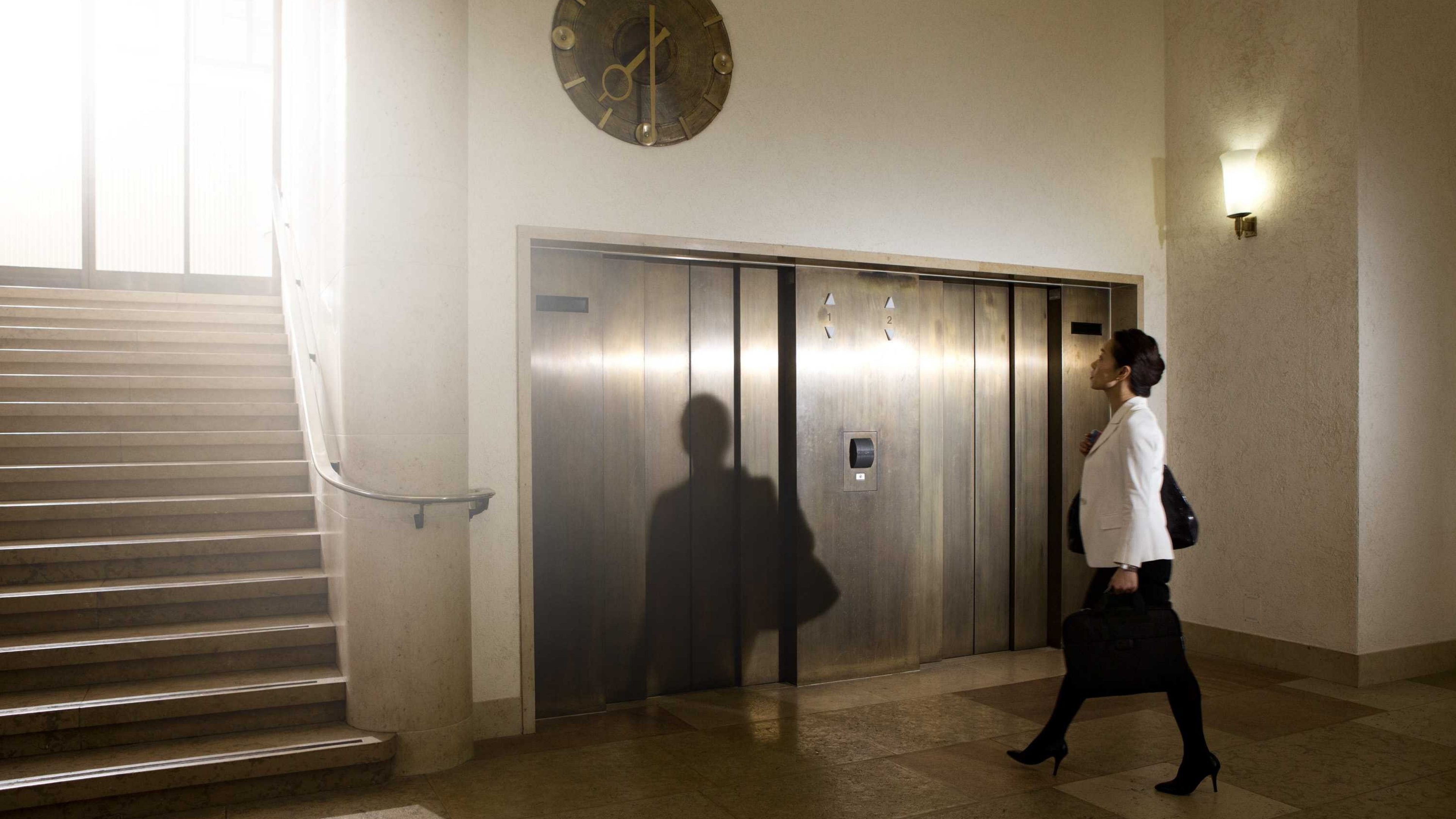 Eine Frau wartet in einem Bürogebäude auf den Aufzug.