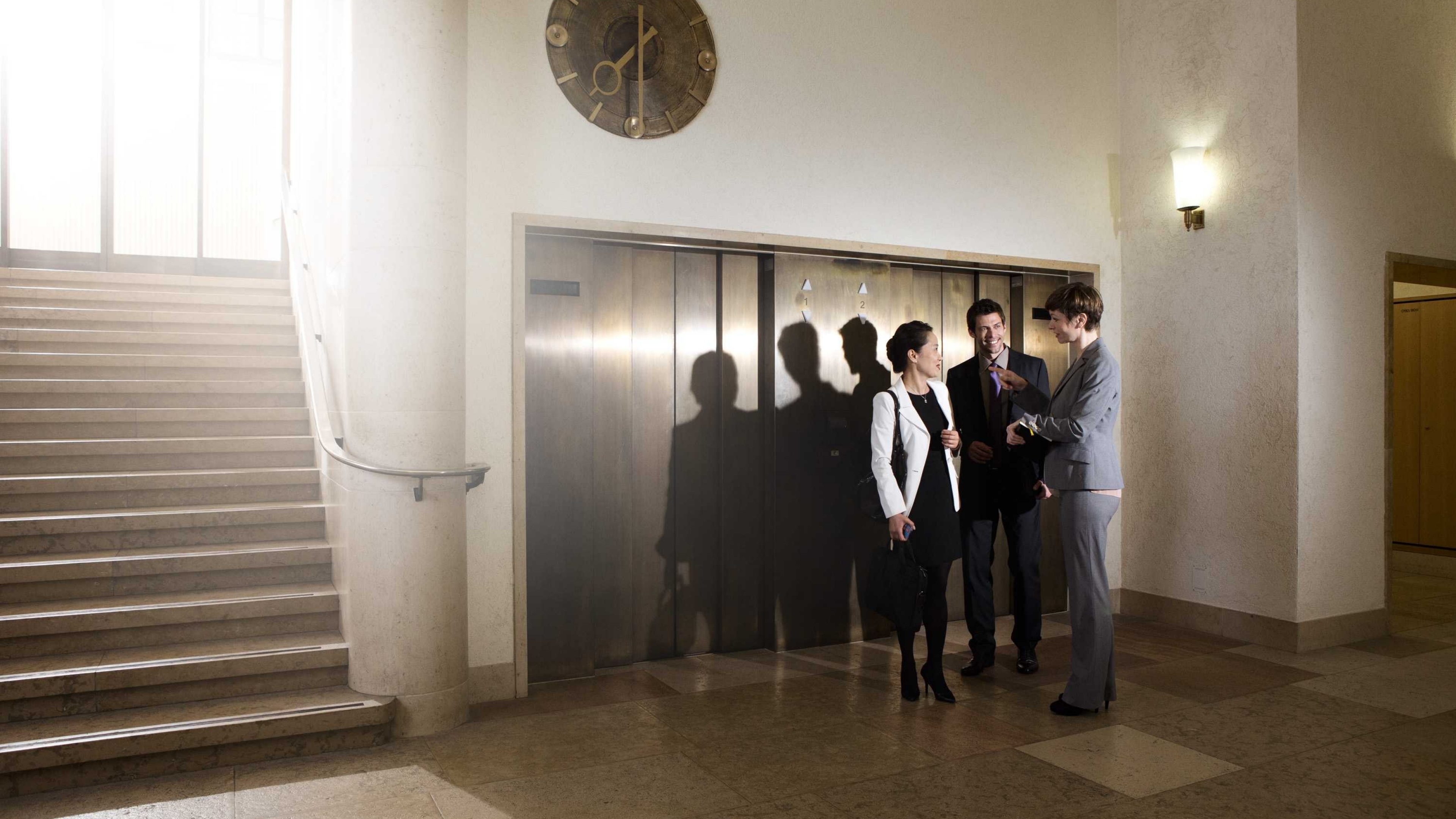 Arbeitskollegen stehen vor dem Aufzug eines Grossunternehmens.