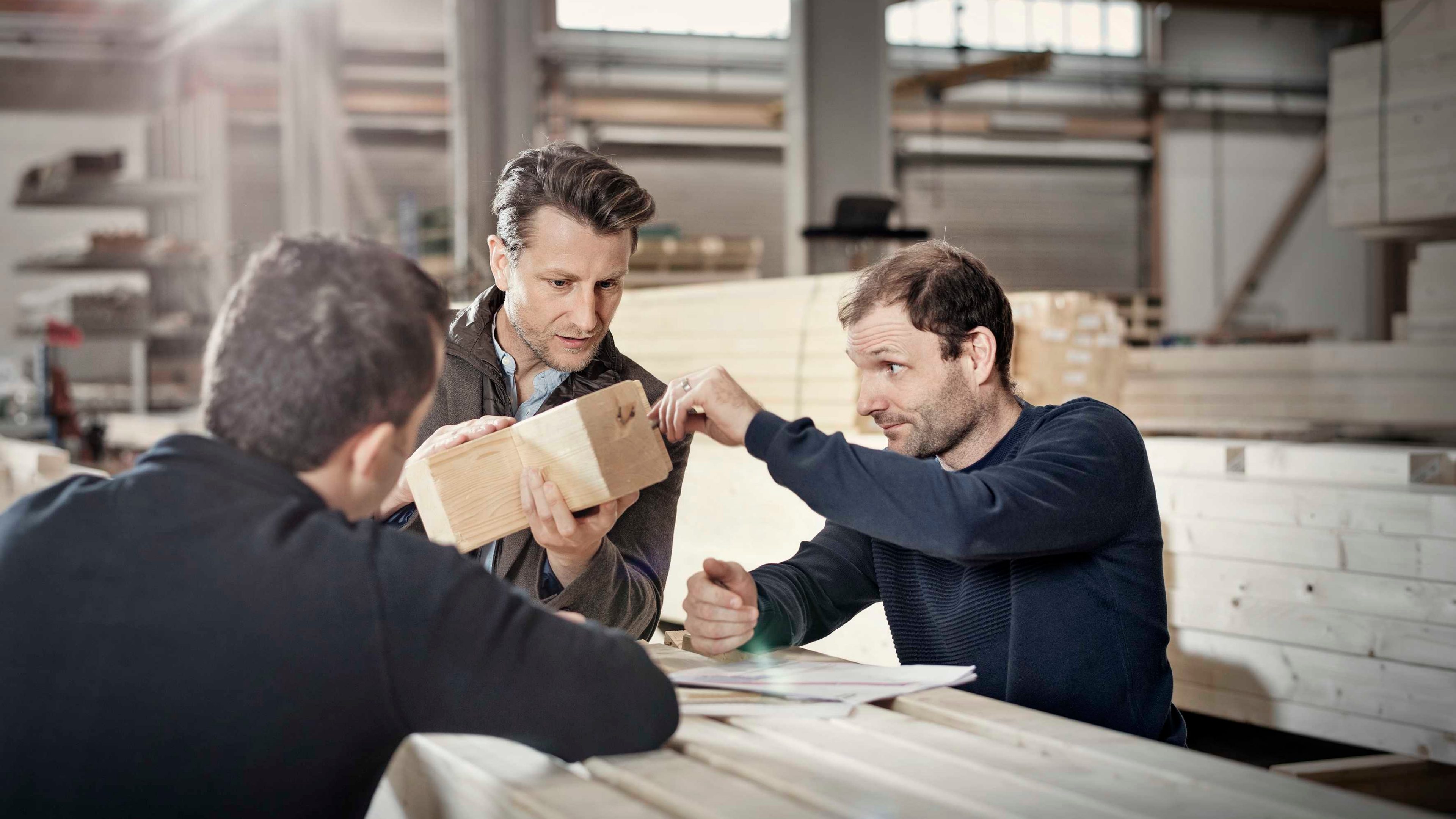 Drei Unternehmer prüfen Holz in ihrer Werkstatt.