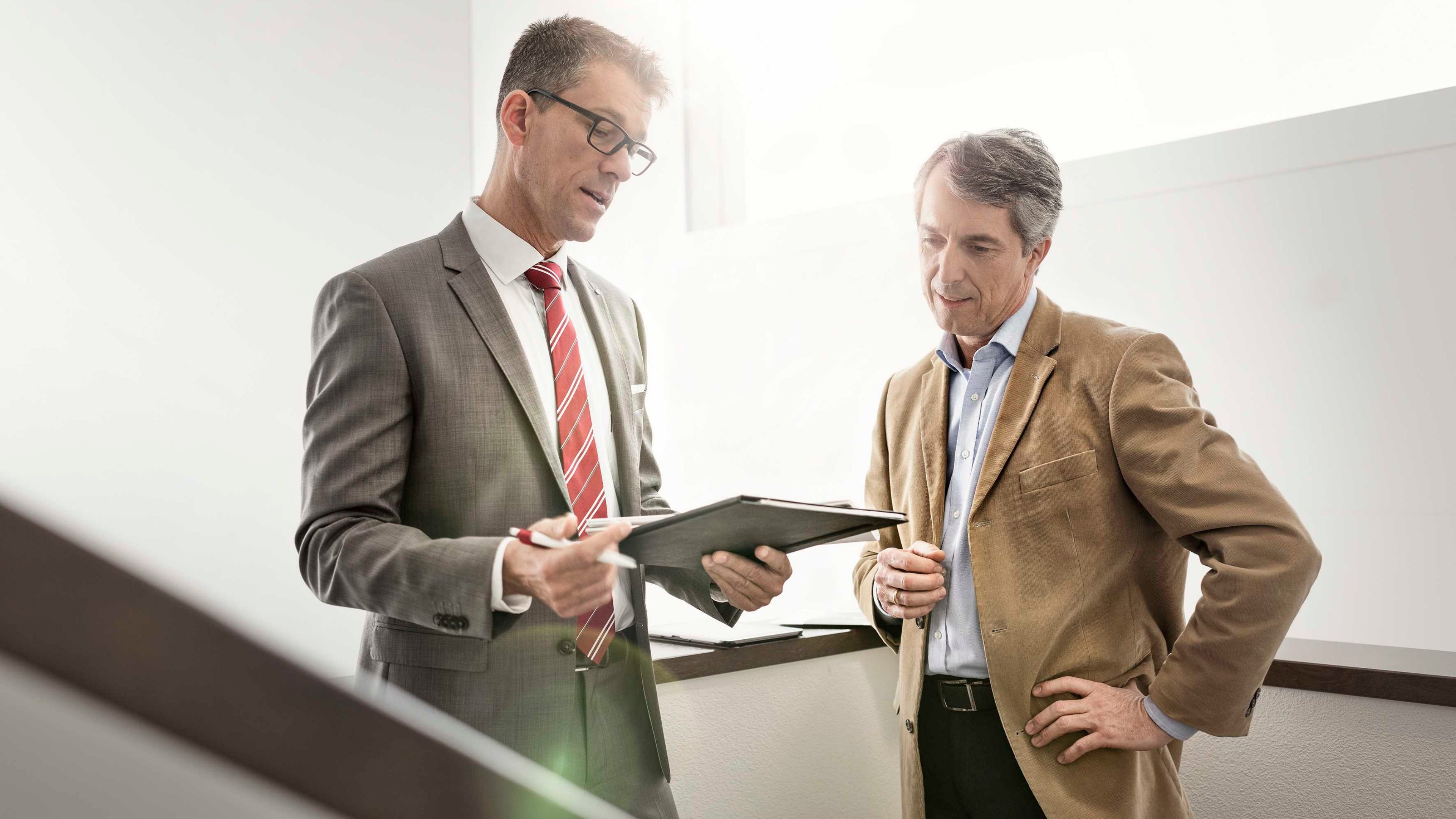 Zwei Arbeitskollegen stehen auf einer Treppe und schauen auf ein Tablet.