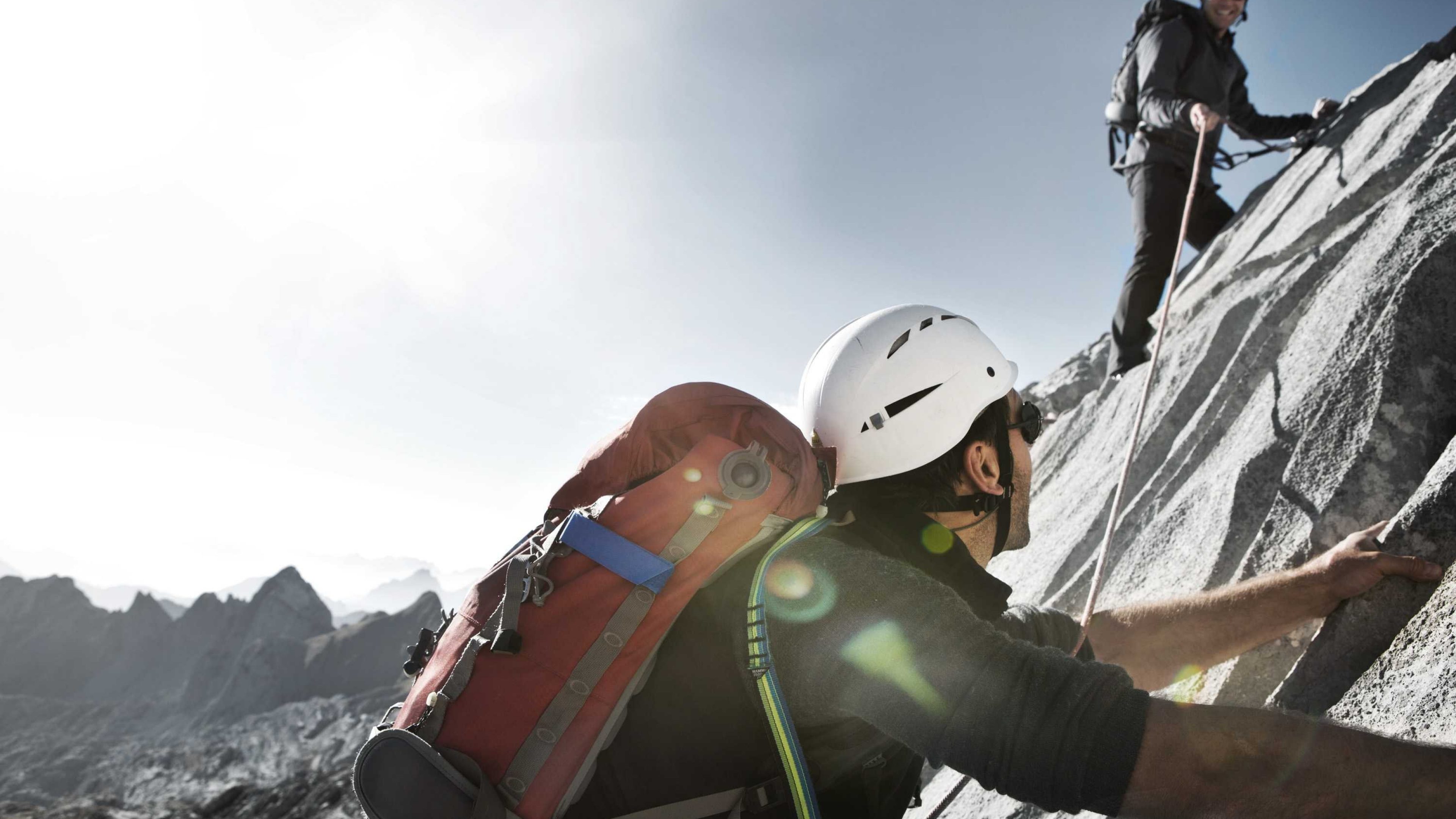 Zwei Bergsteiger mit Ausrüstung klettern an einem Berghang.