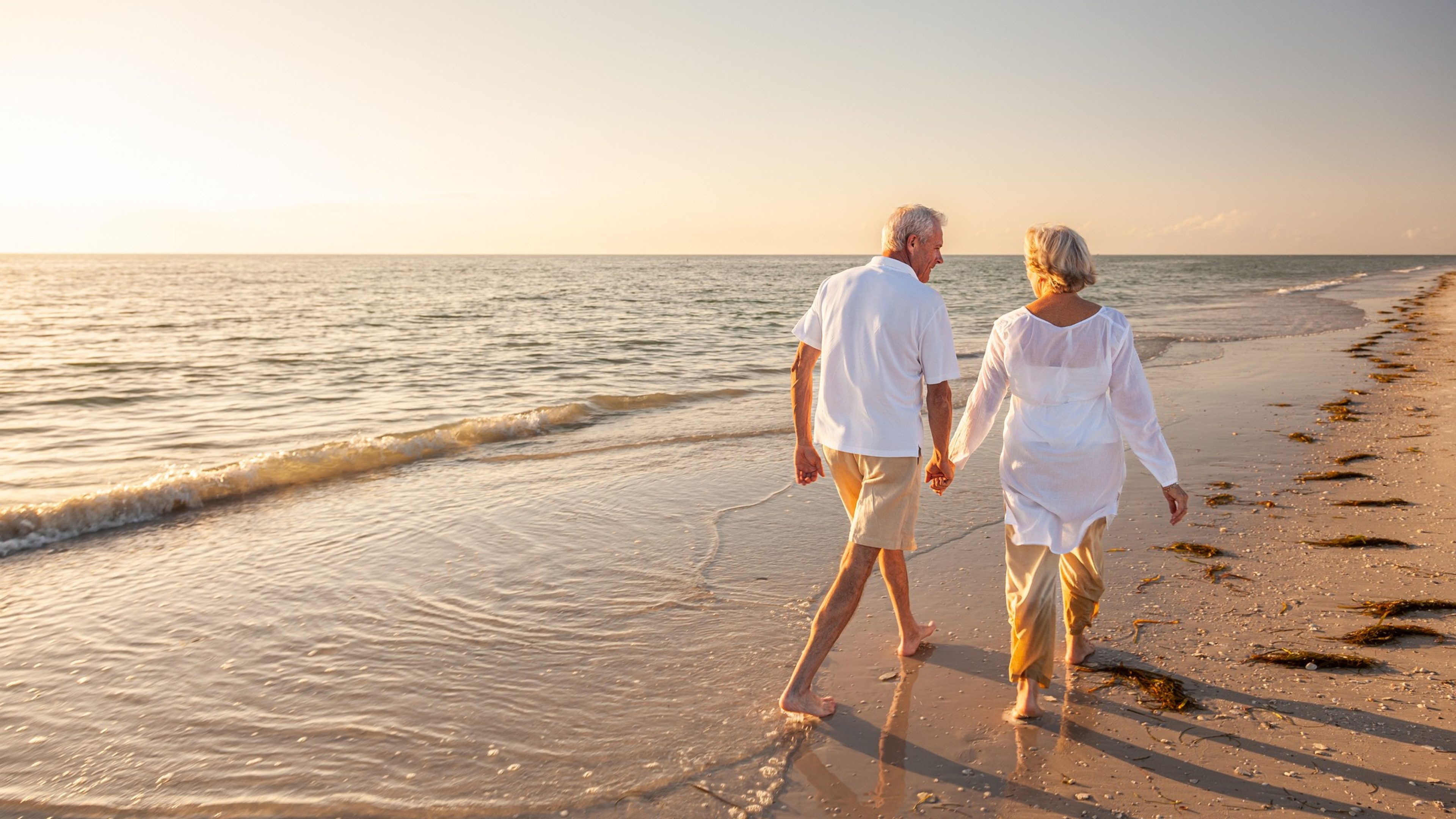 A retired couple walking hand in hand along a beach