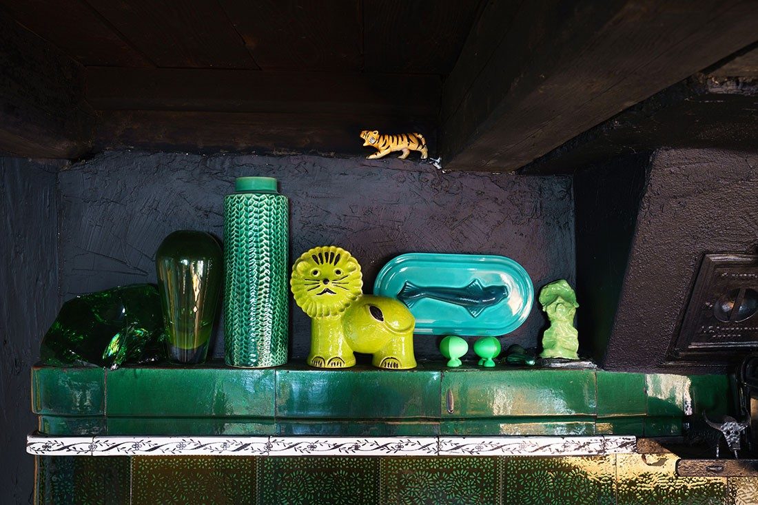 Various decorative objects stand on a green tiled stove bench.